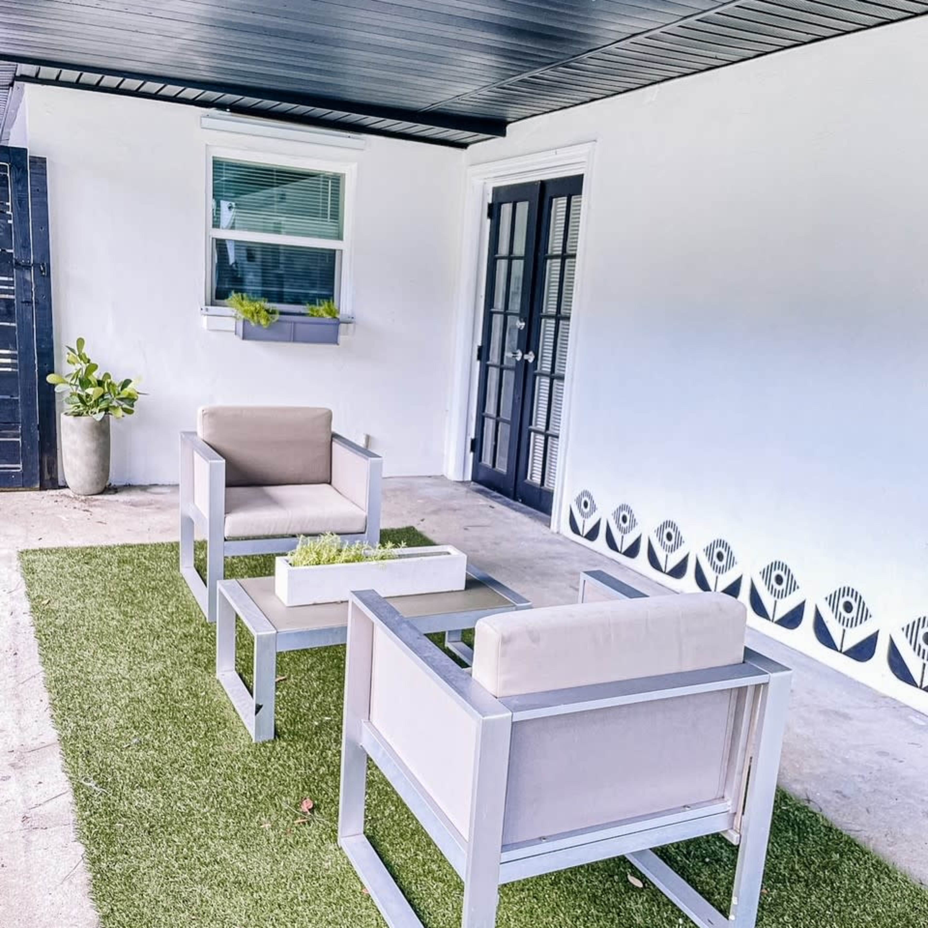 A patio with two modern chairs and a coffee table, all placed on a patch of artificial grass under a covered area.