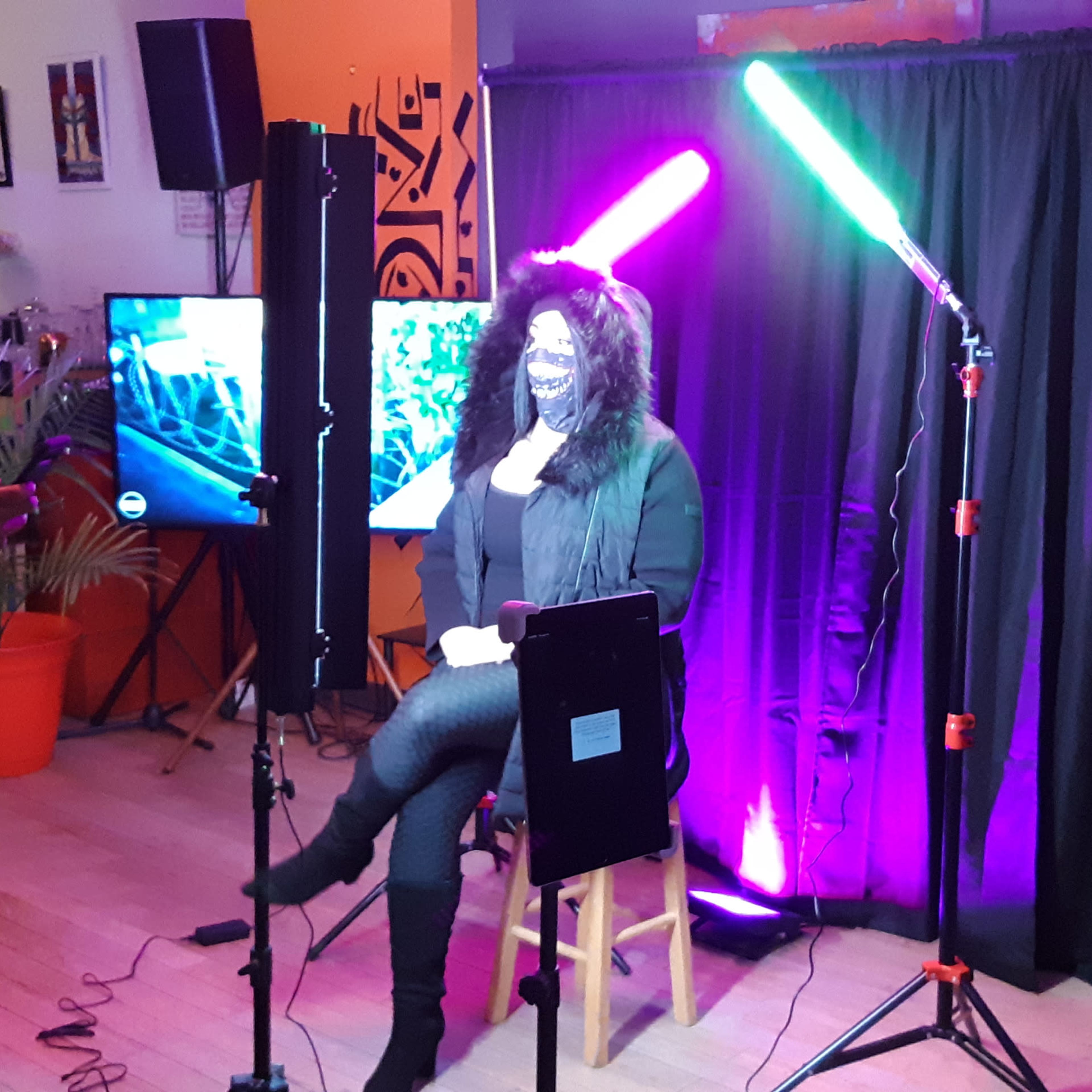 A photographer captures a portrait of a woman seated against a backdrop with colorful lighting, while another person sets up equipment nearby.