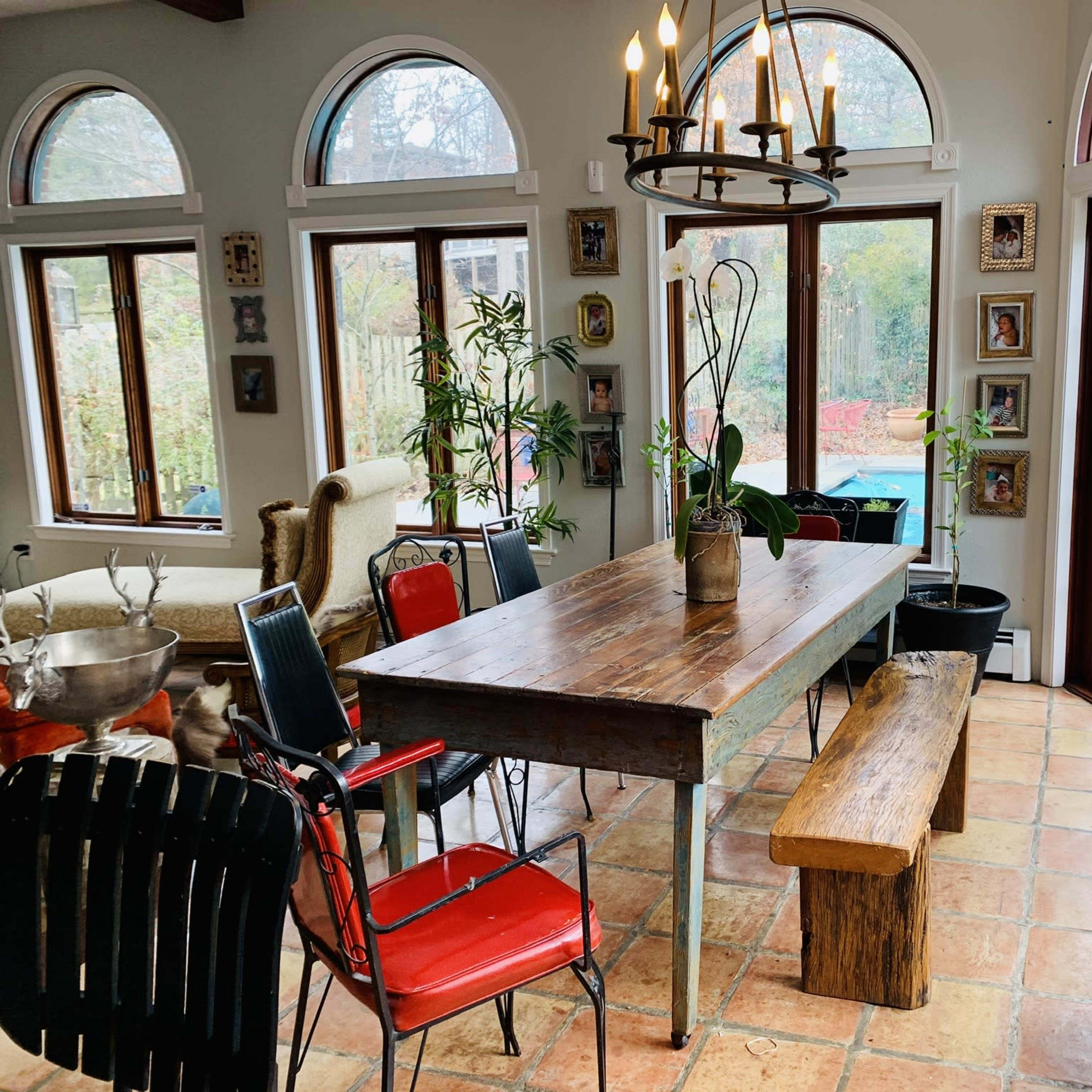 A dining area with a wooden table surrounded by various chairs, a bench, and large windows that overlook a garden.