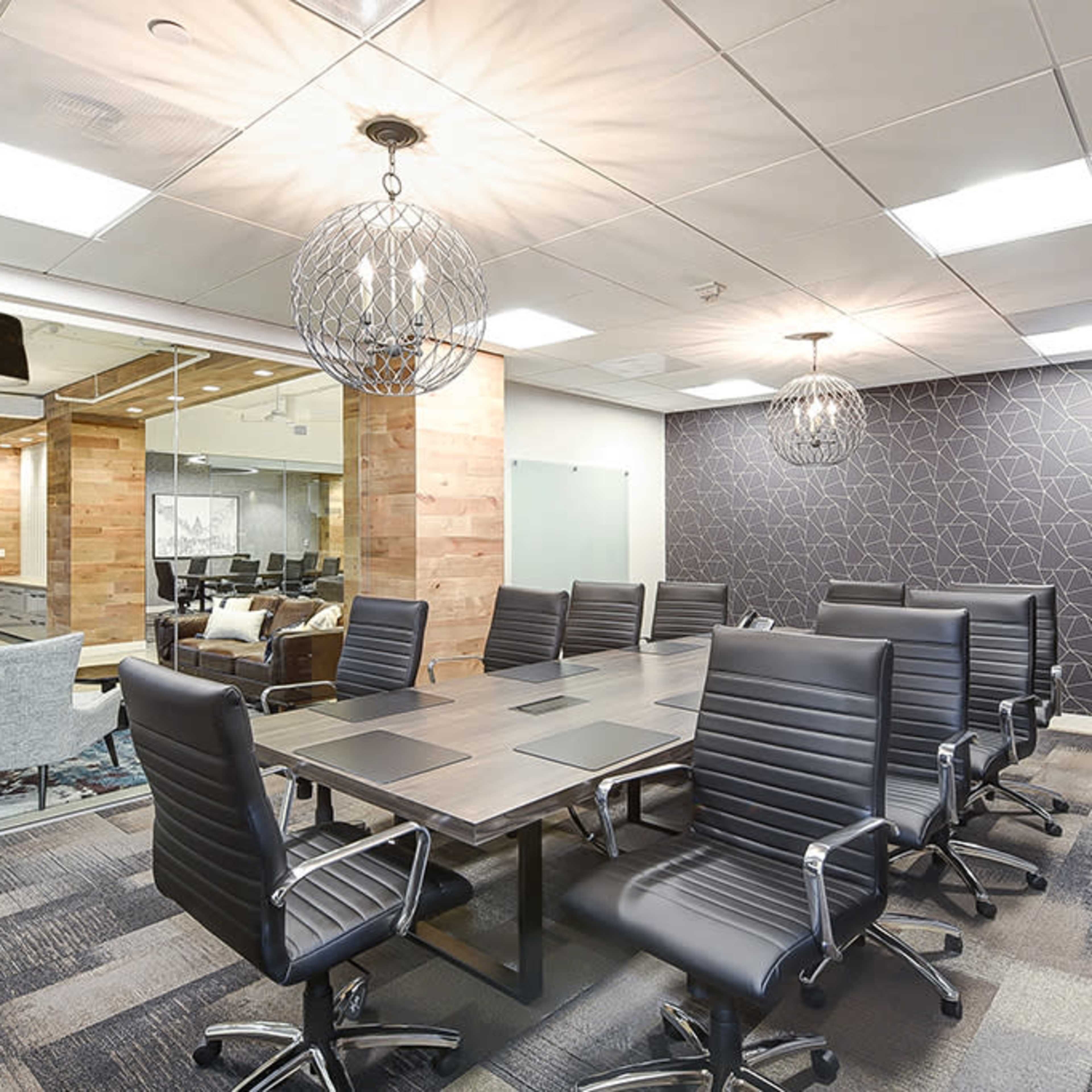 A conference room features a long table surrounded by black chairs, with modern light fixtures and a patterned wall in the background.