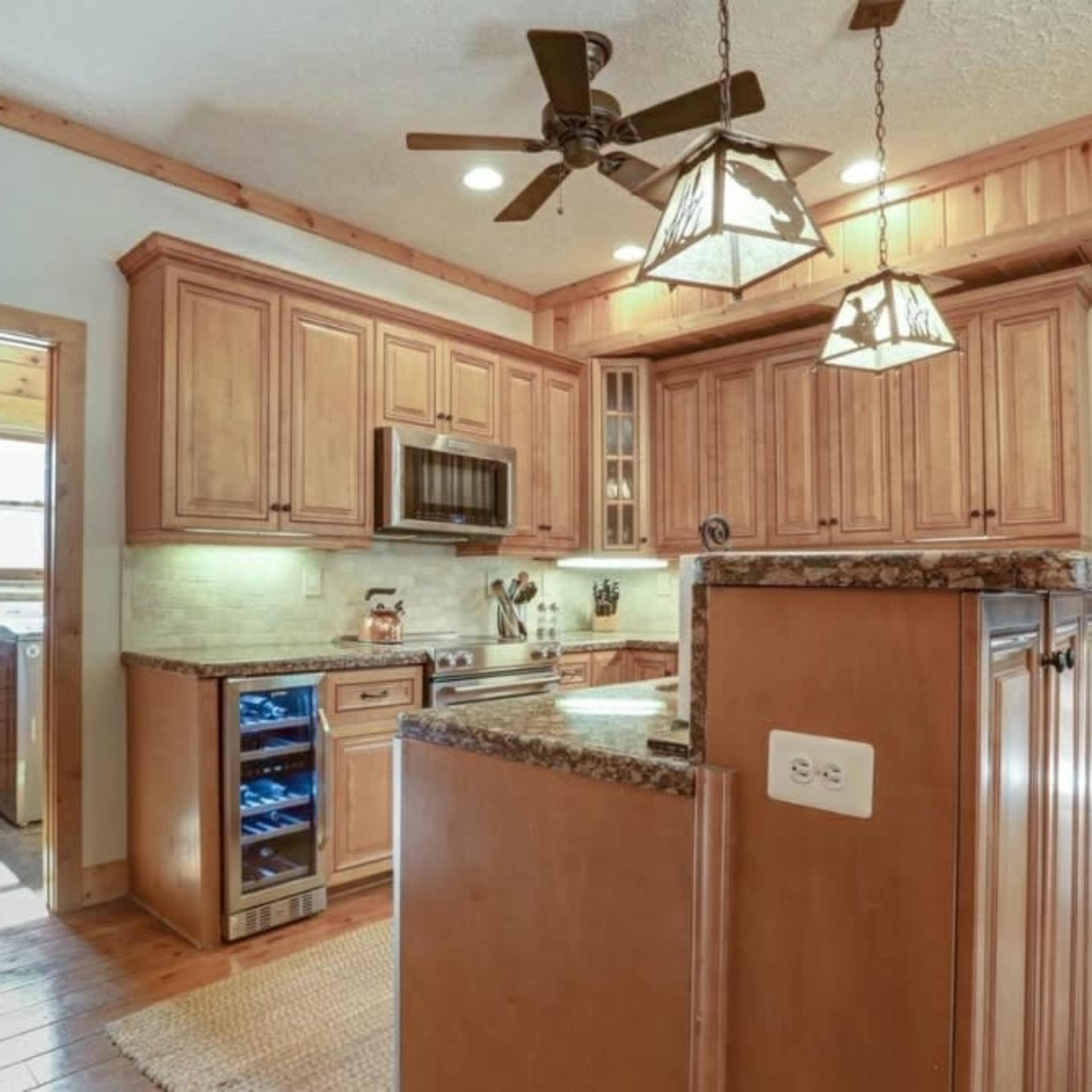 A wooden kitchen with granite countertops, a central island, and overhead pendant lights.