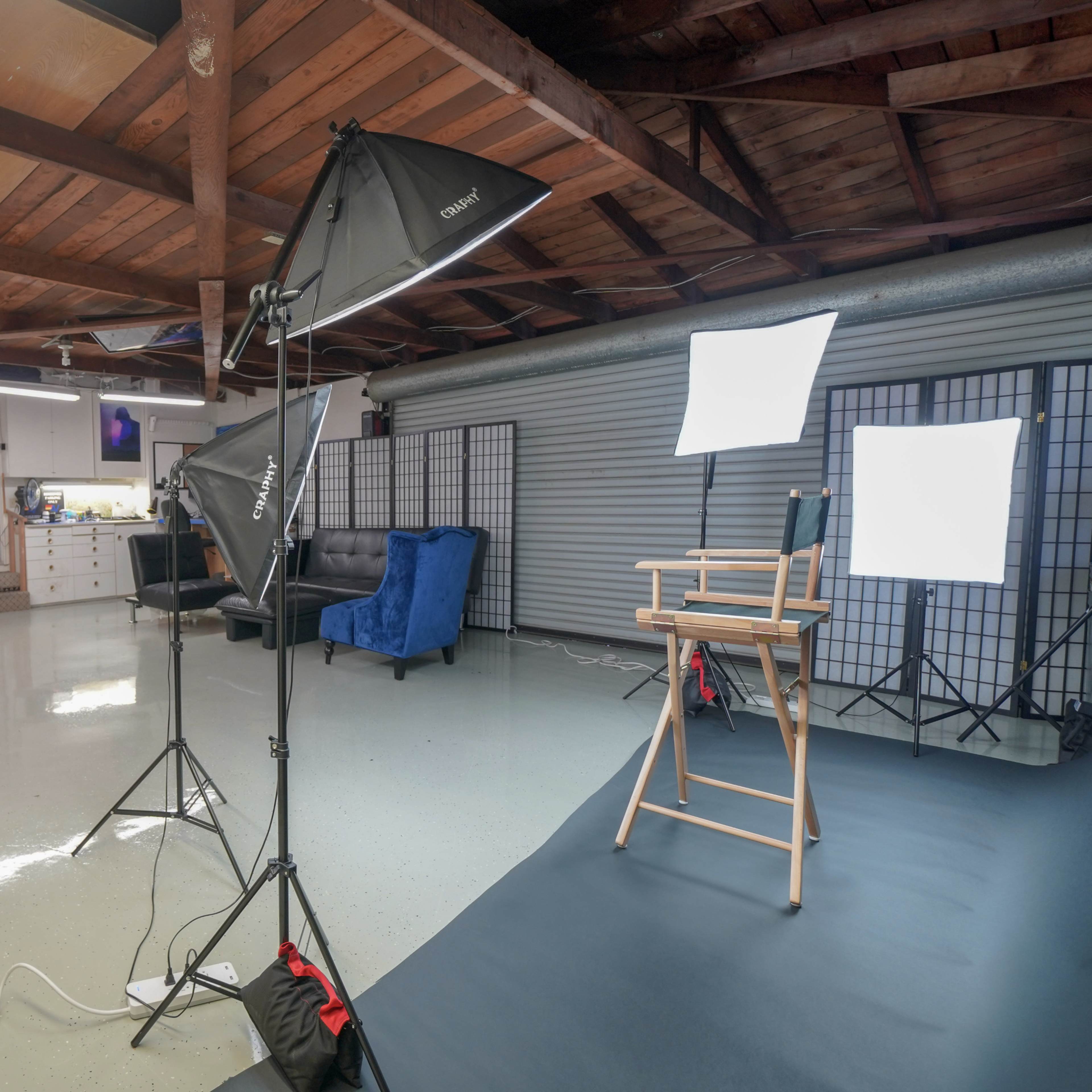 A well-lit studio space with a wooden ceiling, equipped with photography lighting, empty director's chairs, and a blue couch.