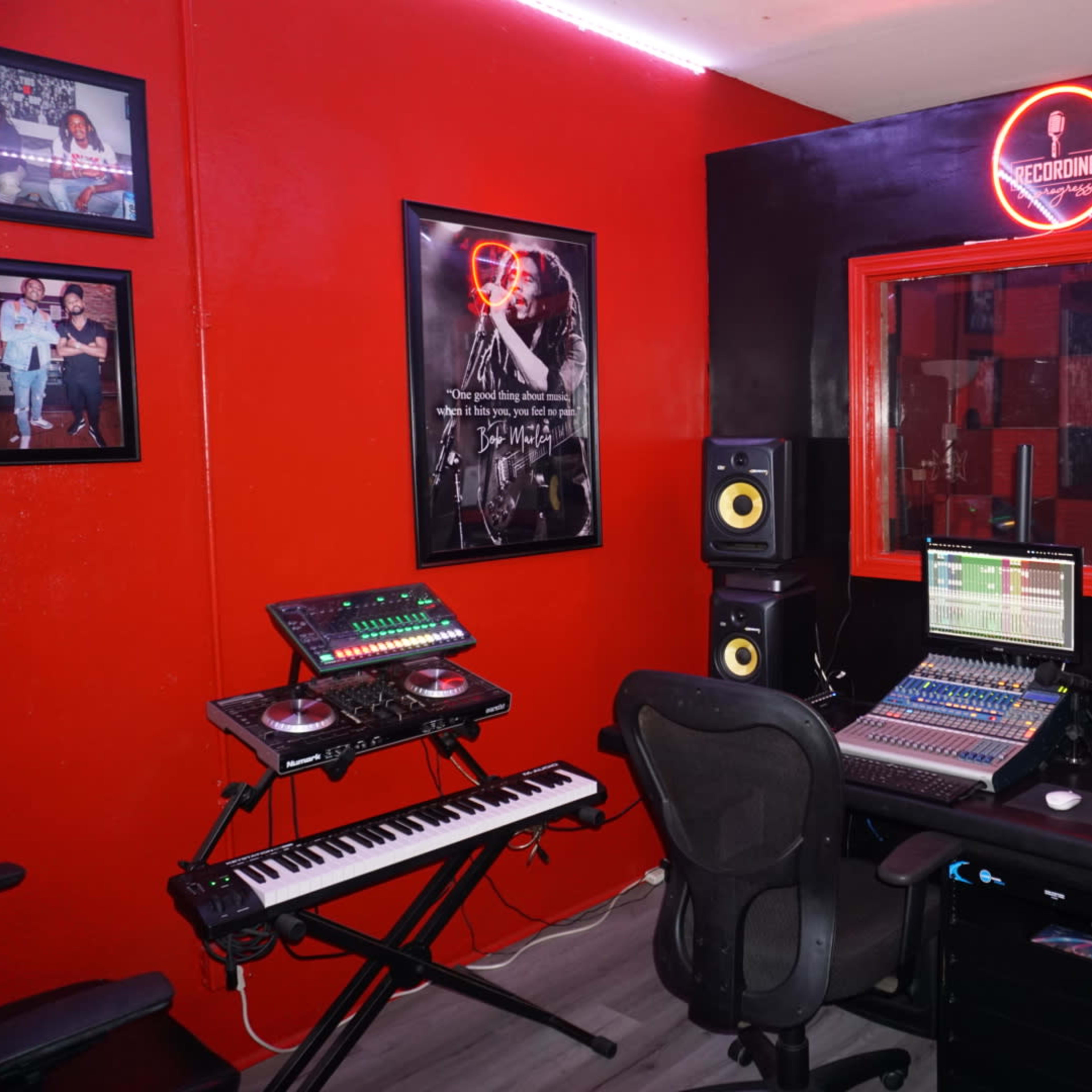 A music recording studio featuring a black and red color scheme, equipped with audio equipment, speakers, and framed photographs on the walls.