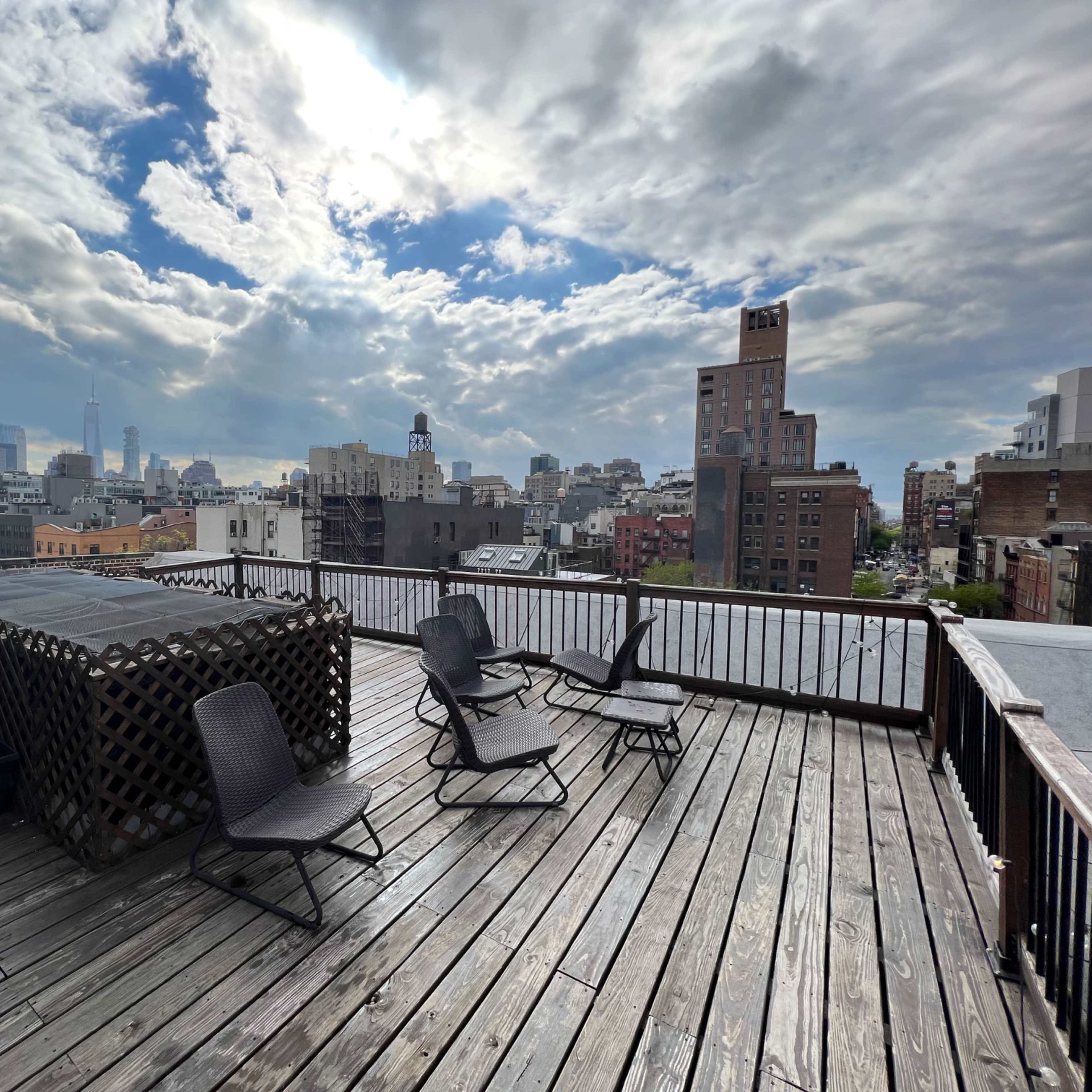 A rooftop deck with several black chairs facing a skyline that includes tall buildings and cloudy skies.