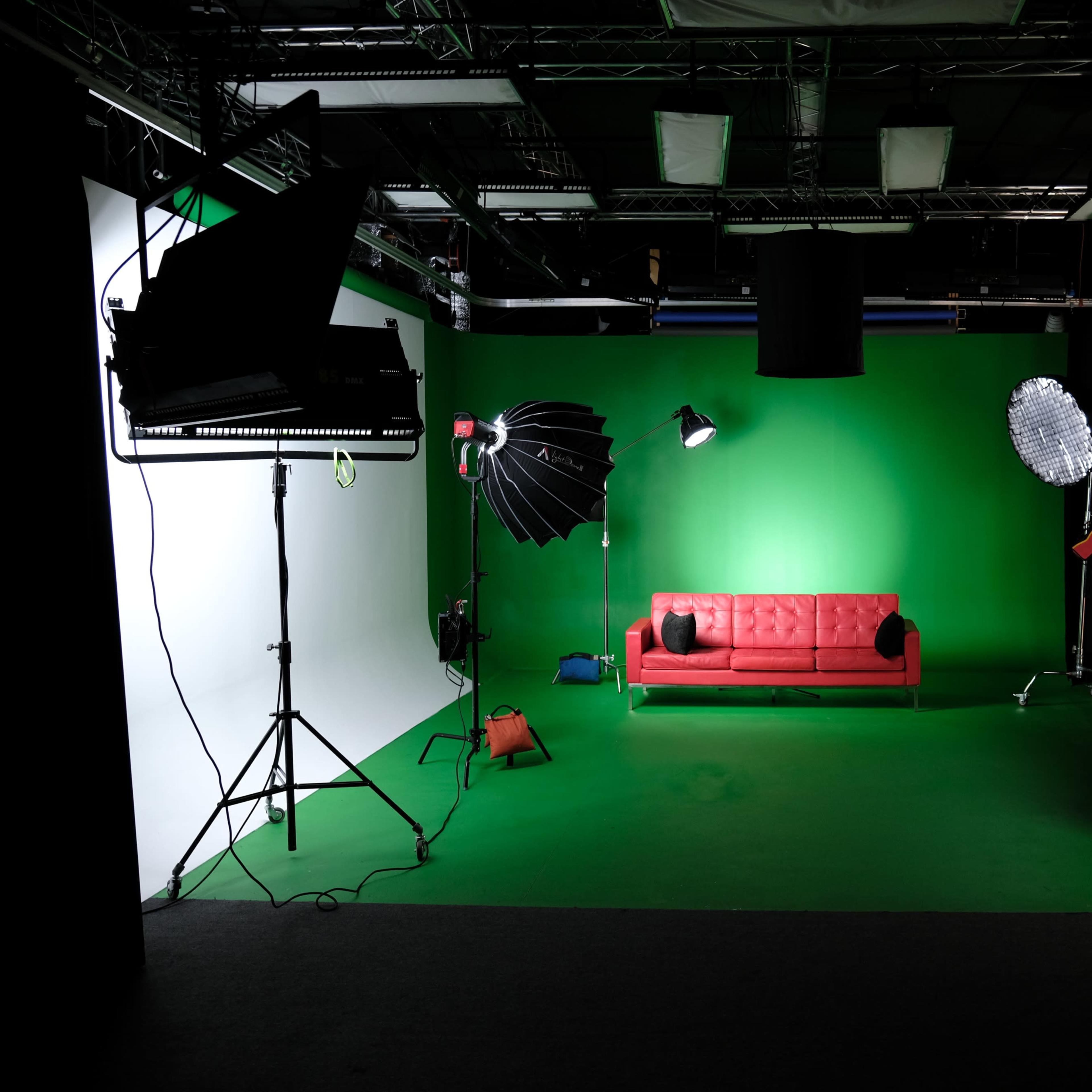 A television studio with a green backdrop, a red couch in the center, and various lighting equipment arranged around the space.