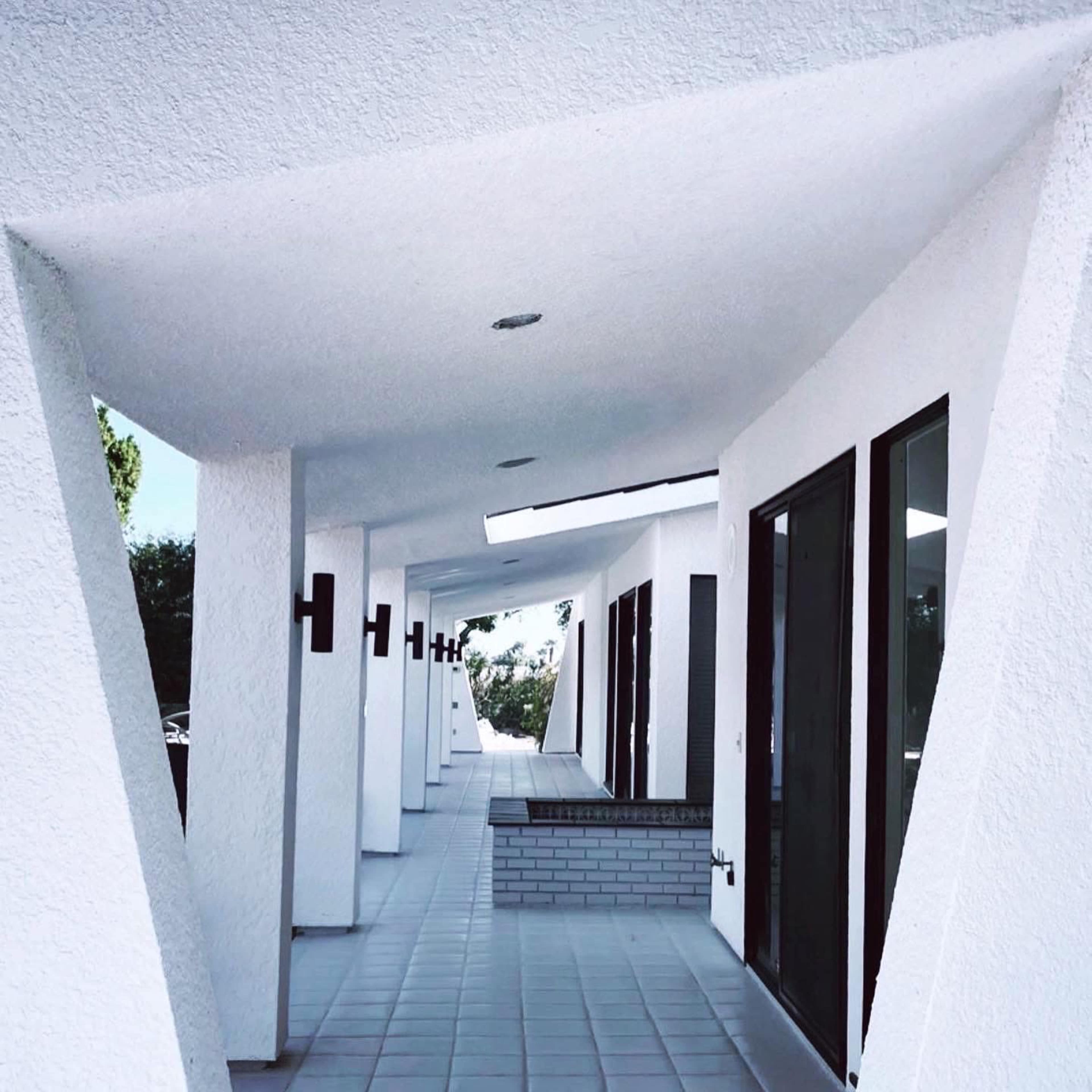 A series of white columns supporting a roof, creating a covered walkway with large windows along one side.