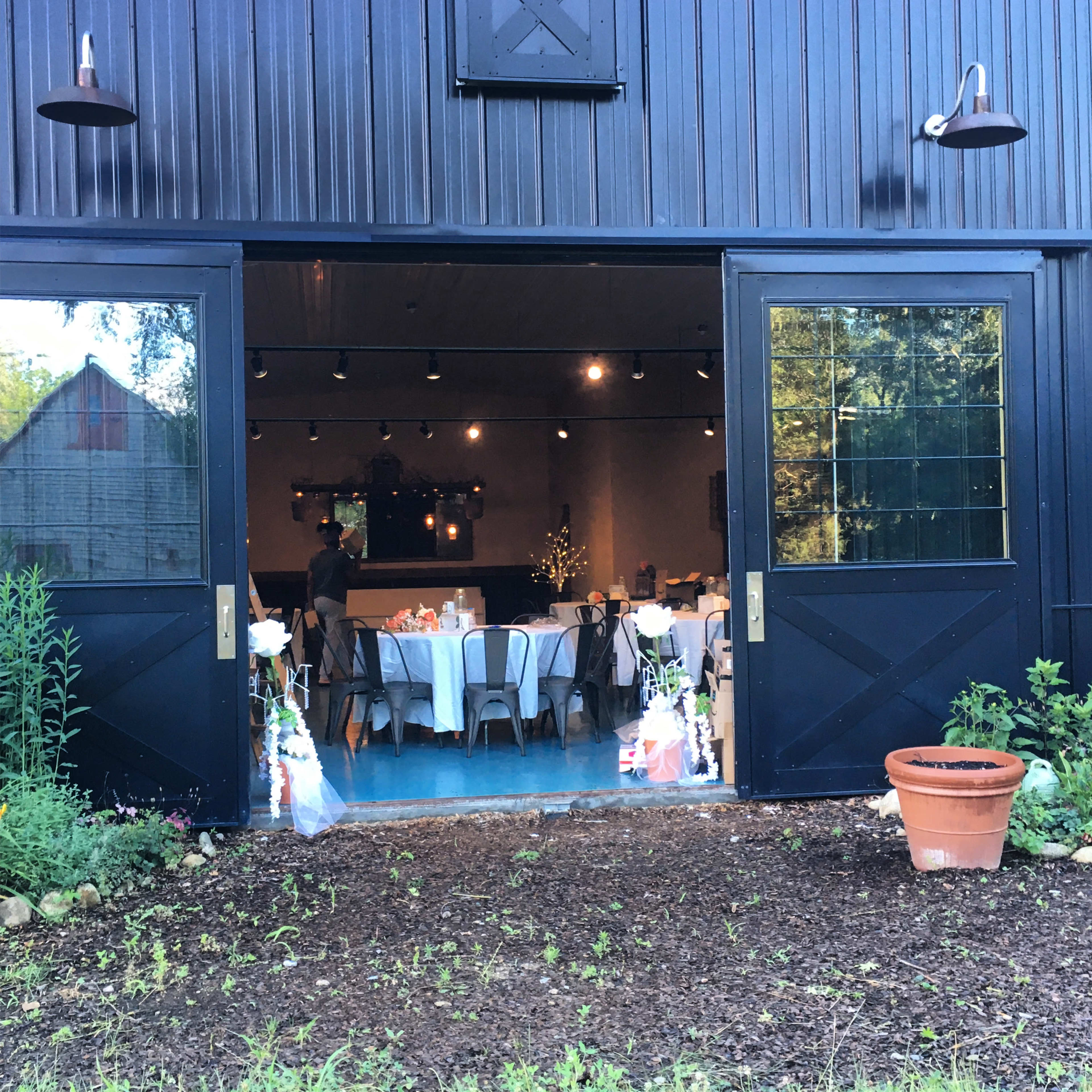 A large barn-style venue is set up for an event, with tables arranged inside and decorative flowers at the entrance.