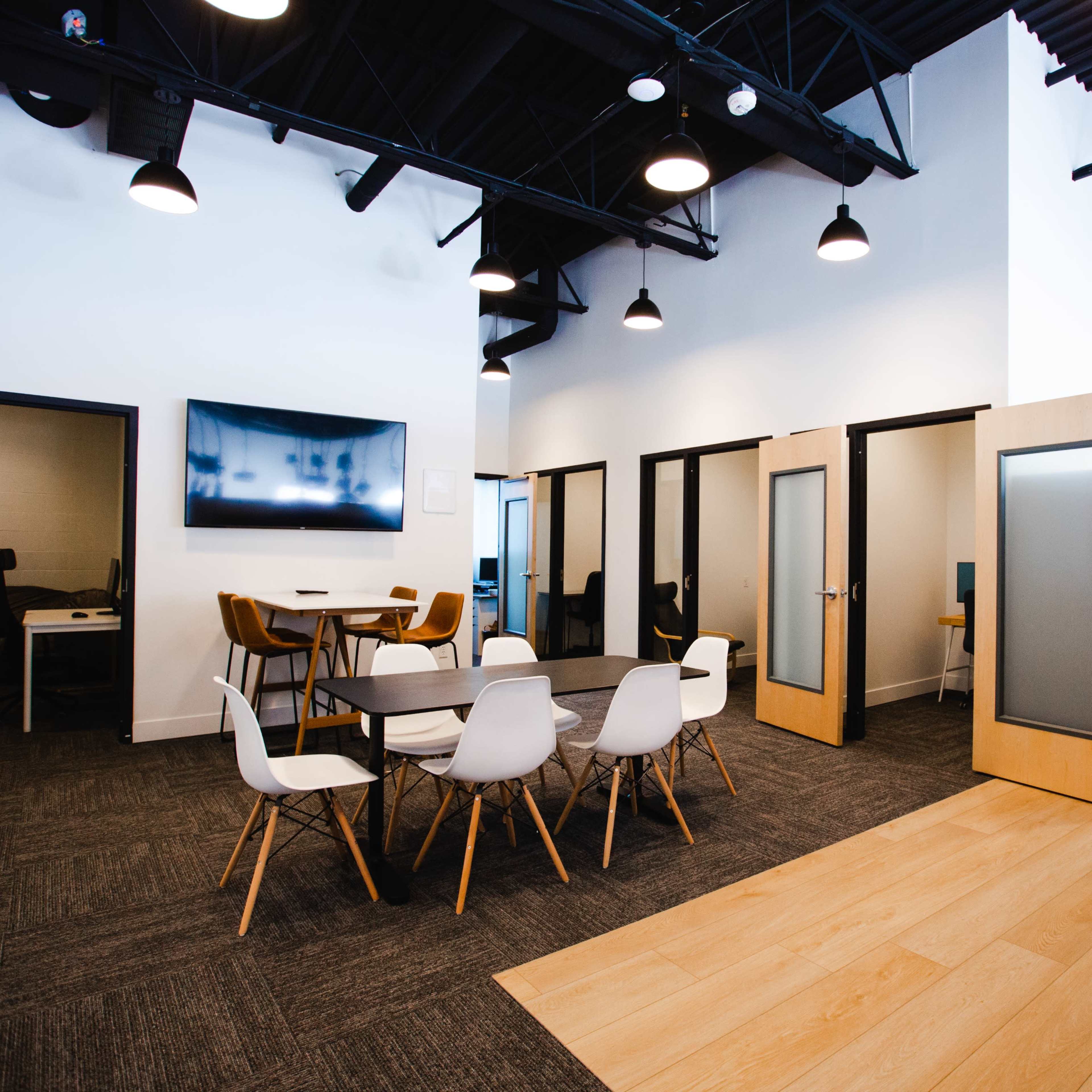 A modern office space featuring a large table with white chairs, open cubicles, and frosted glass doors.