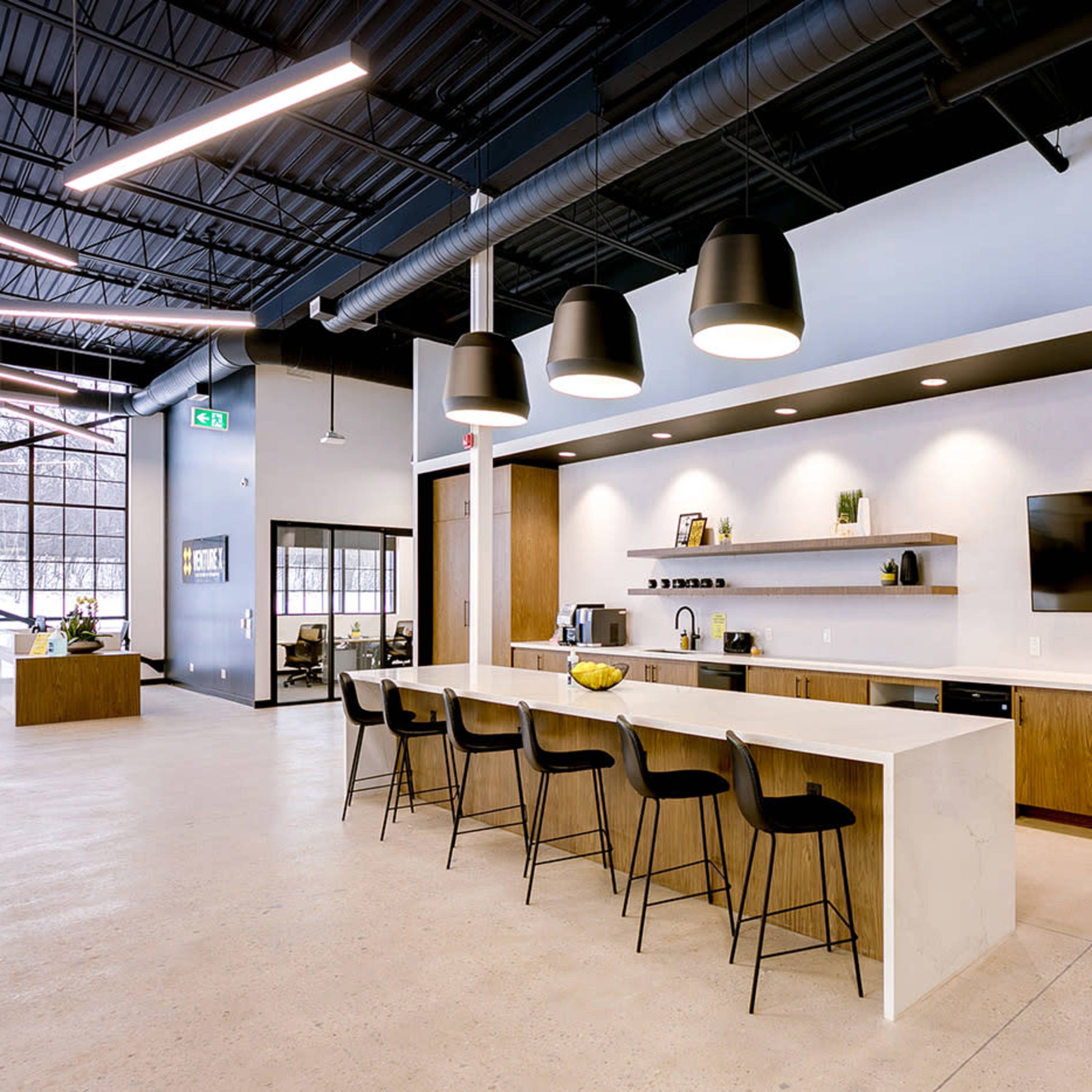 A modern kitchen area with a long counter, high stools, and a wall-mounted television.