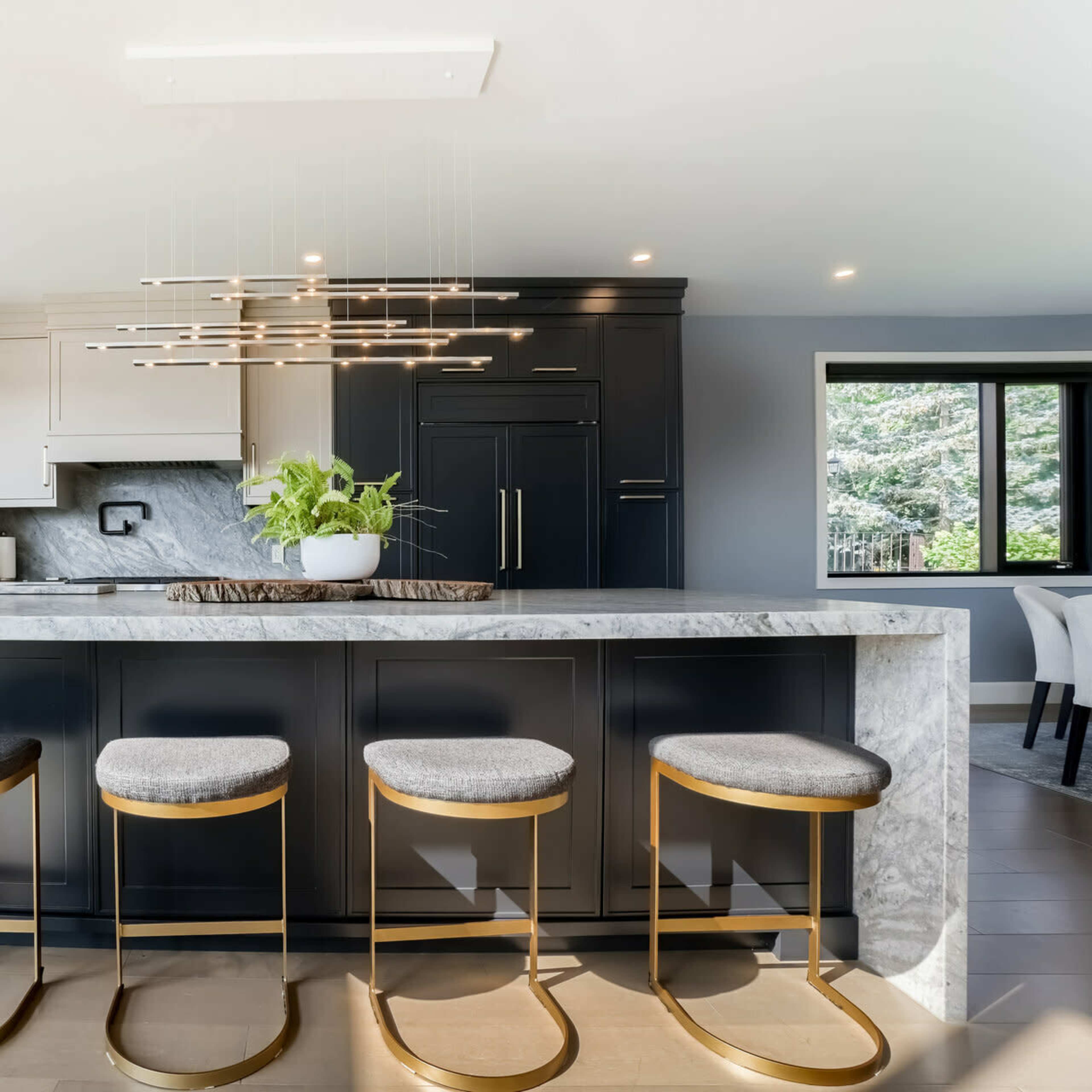 A modern kitchen featuring a large marble island with four gold-accented bar stools and sleek black cabinets.