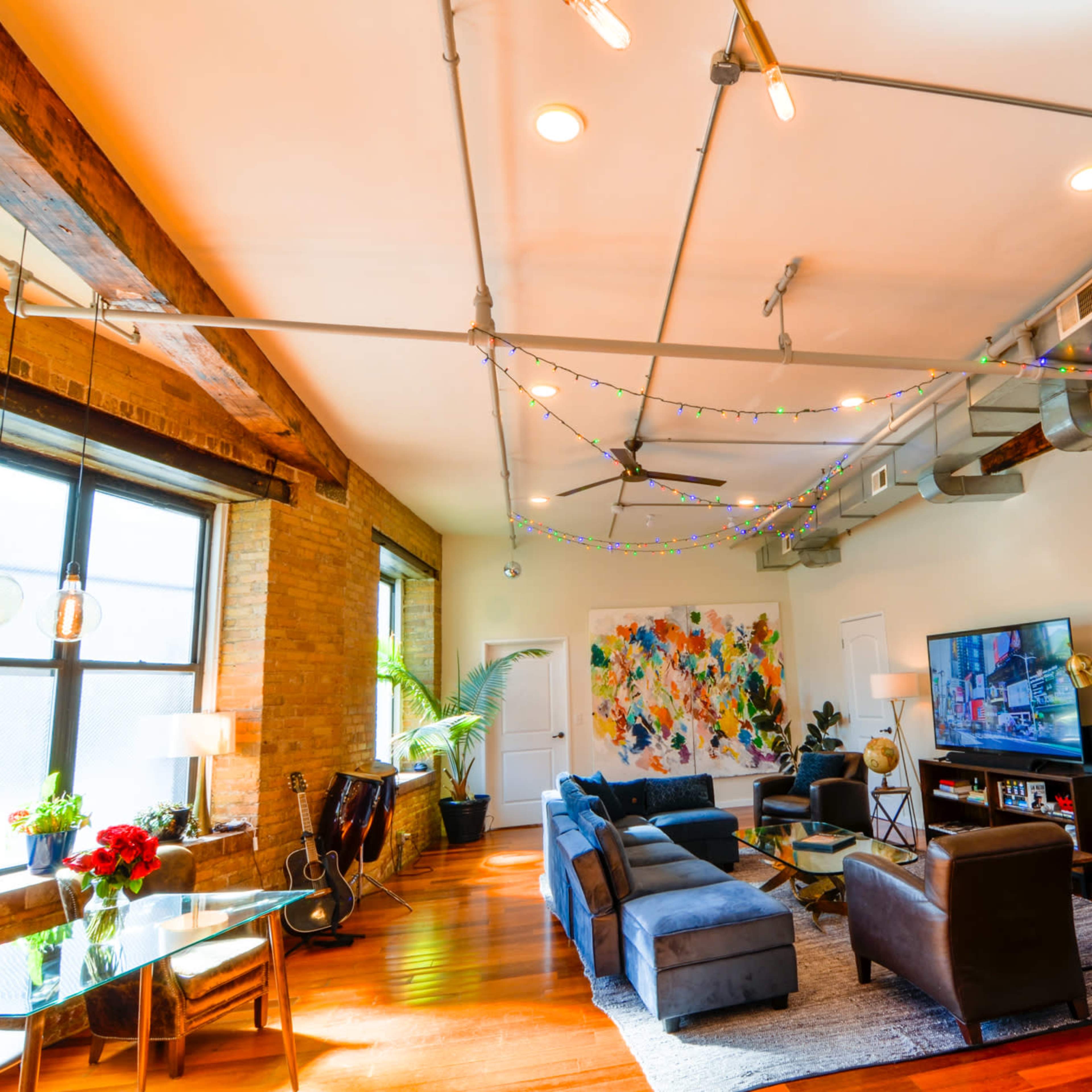A spacious living room featuring modern furniture, exposed brick walls, and decorative string lights hanging from the ceiling.