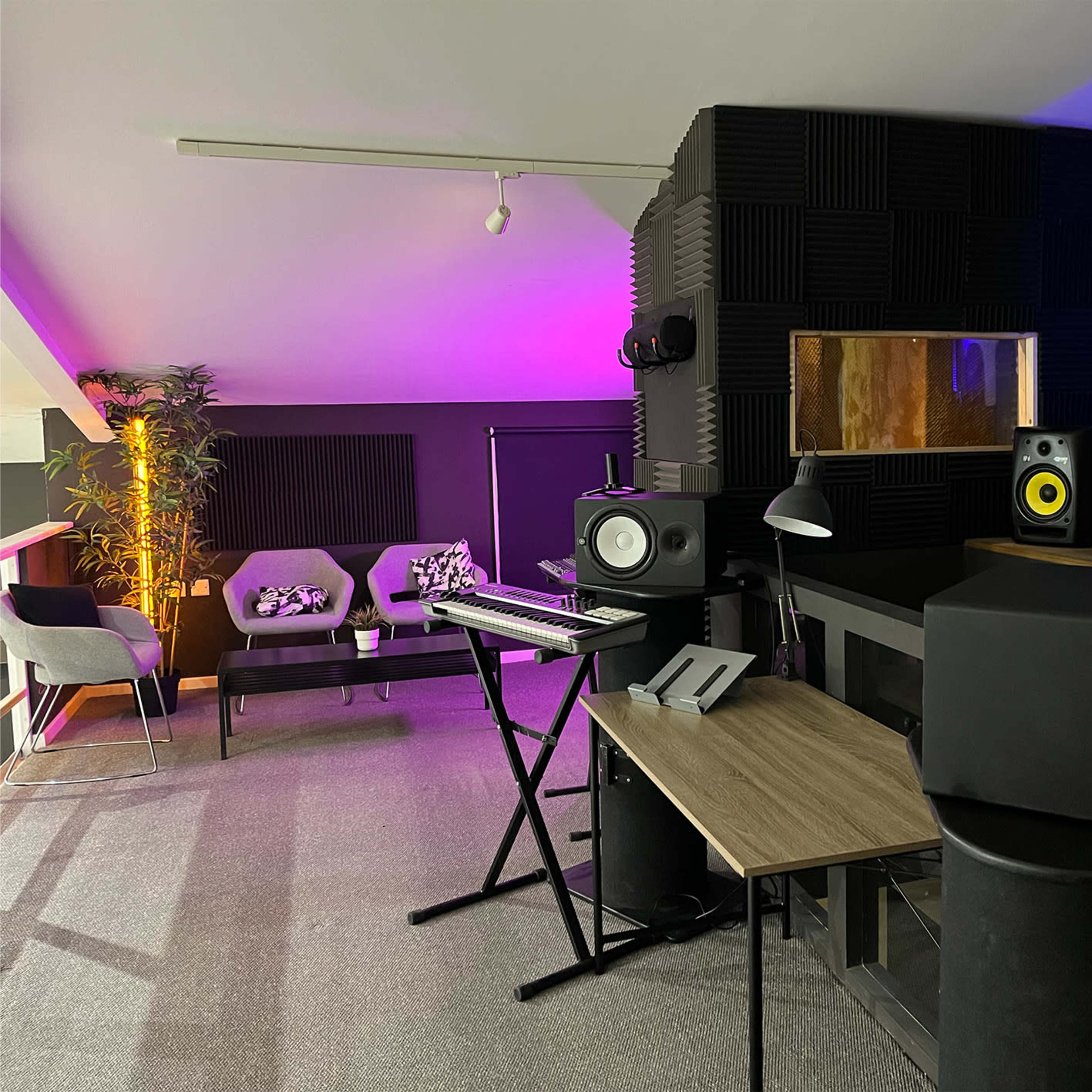 A music production studio features a desk with equipment, acoustic panels on the walls, and ambient lighting.