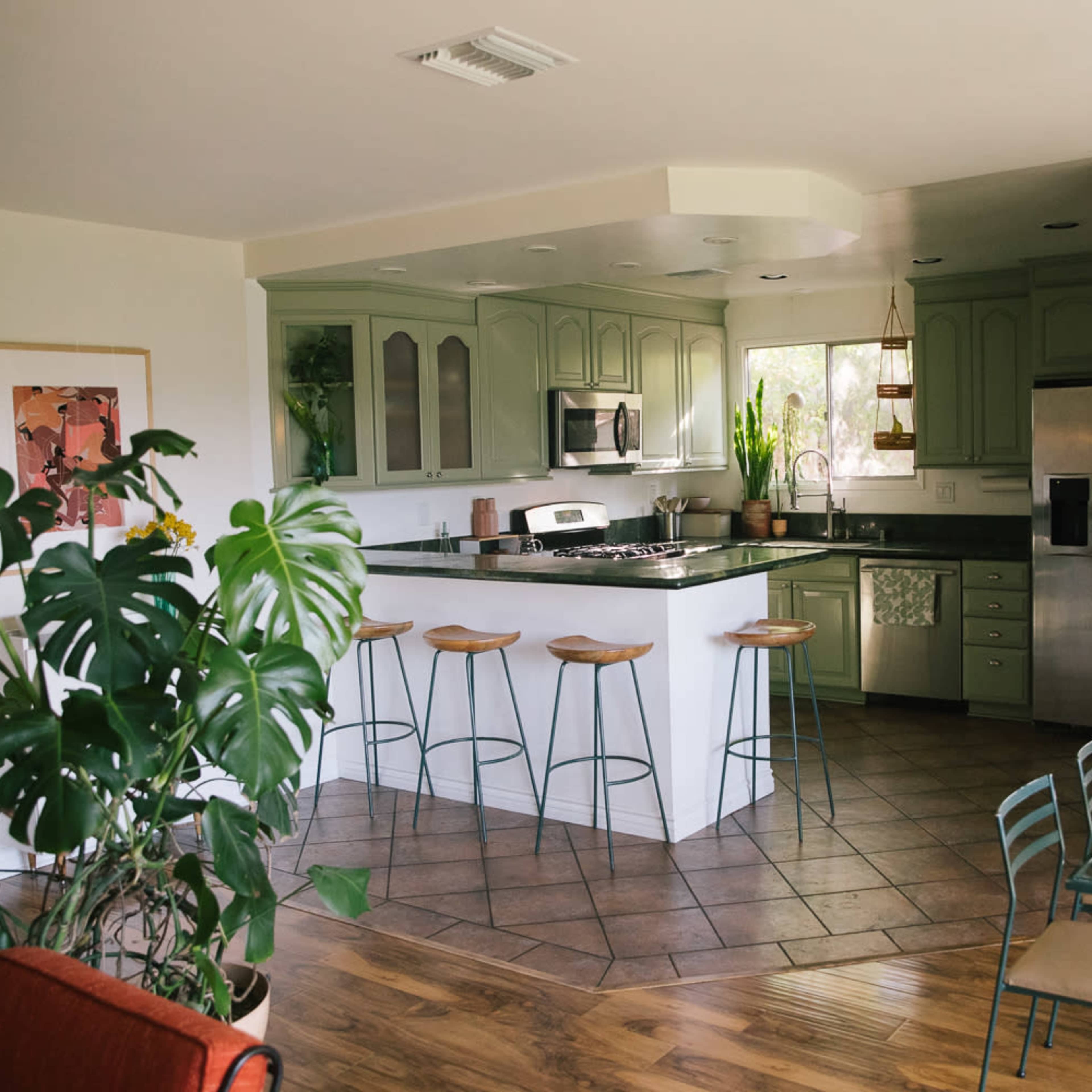 A modern kitchen featuring light green cabinets, stainless steel appliances, and a dining area with a glass table and metal chairs.