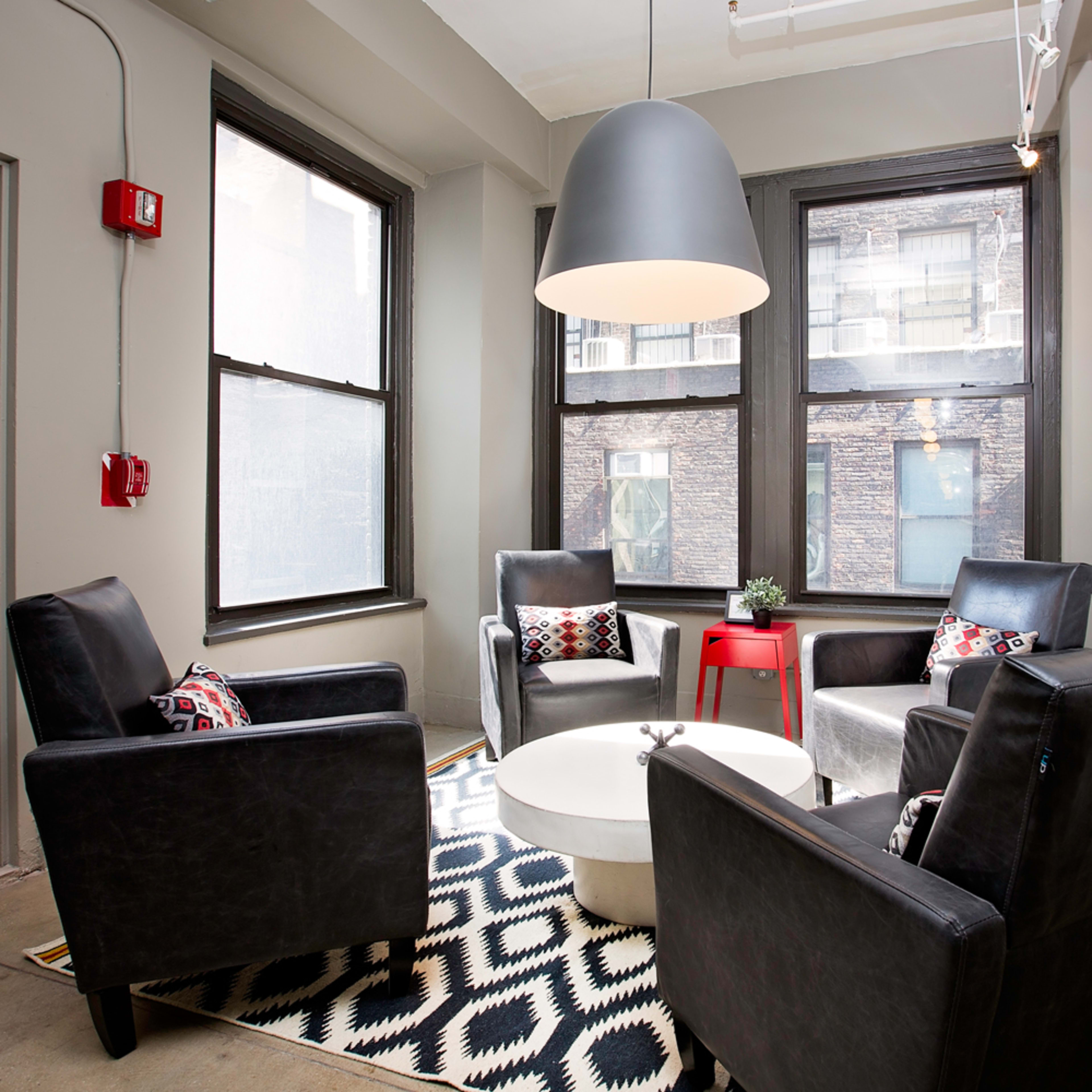 A modern seating area with four black chairs arranged around a circular coffee table, positioned on a patterned rug under a large pendant light.