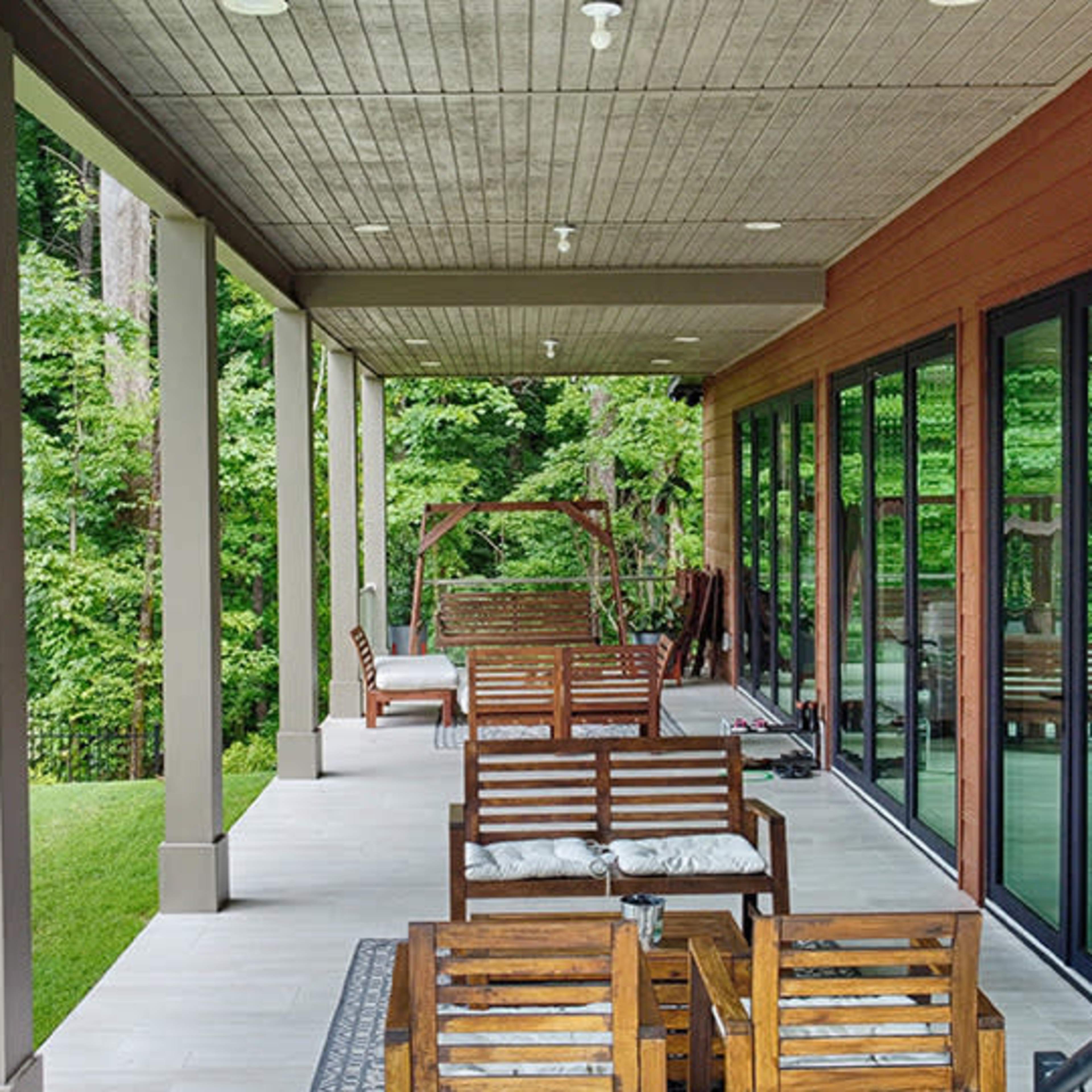 A spacious outdoor patio features wooden seating arranged along a covered area, surrounded by greenery.