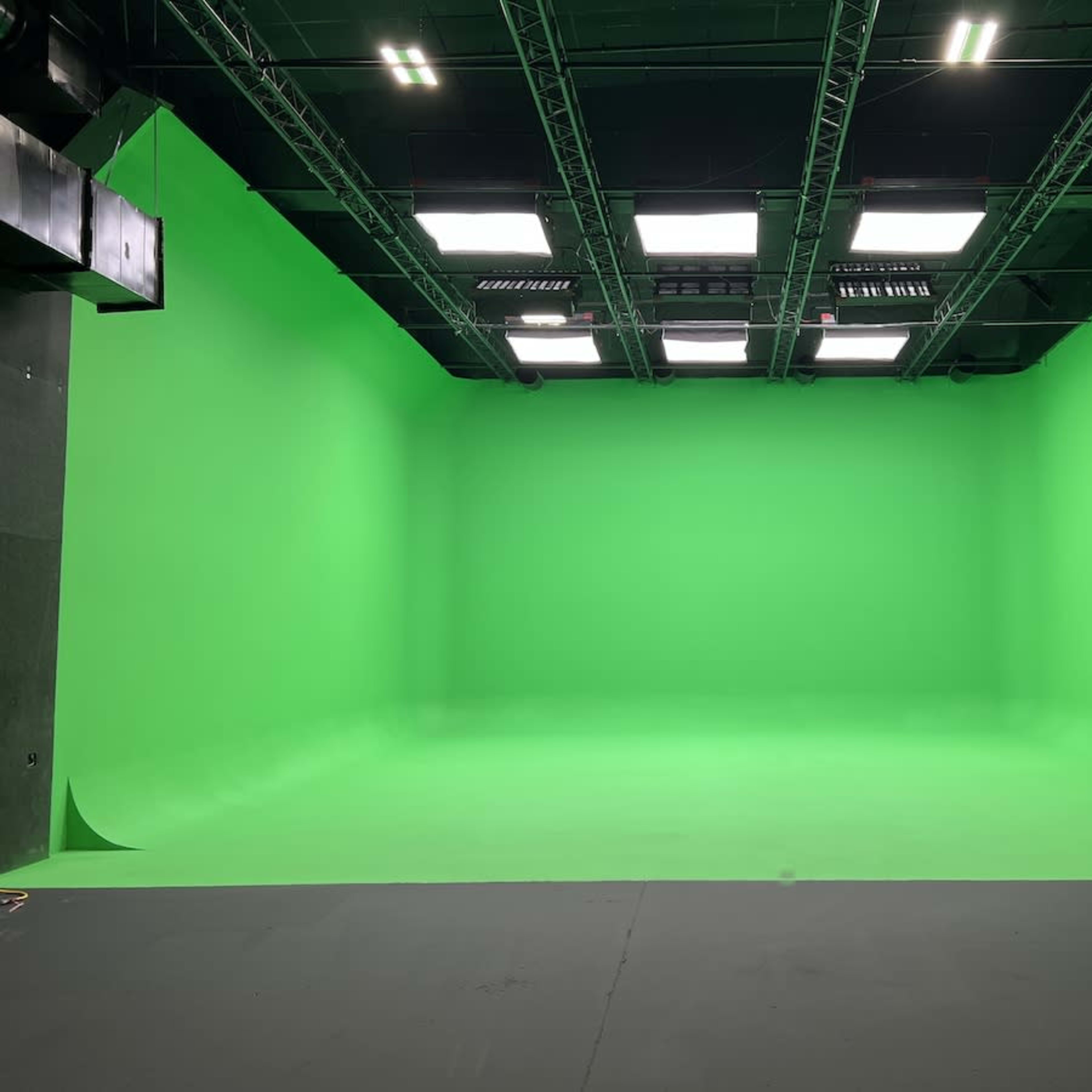 A large green screen studio with a seamless green backdrop and overhead lighting.