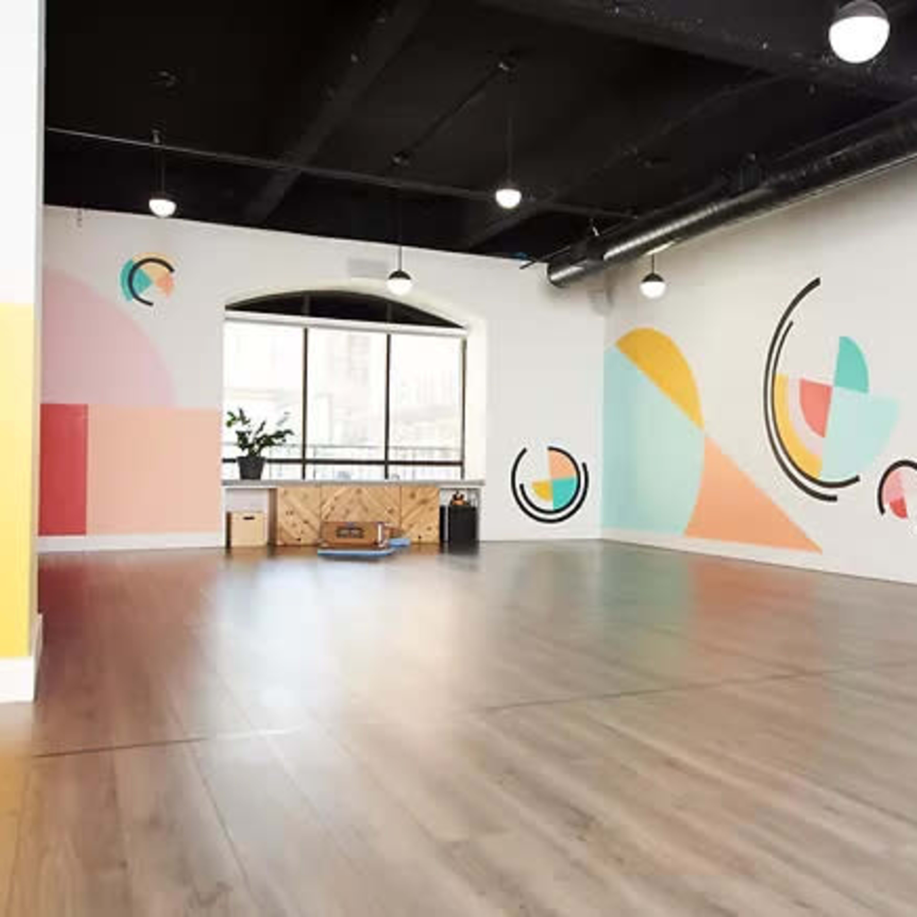 An empty room with wooden flooring and a decorative wall featuring colorful abstract shapes.