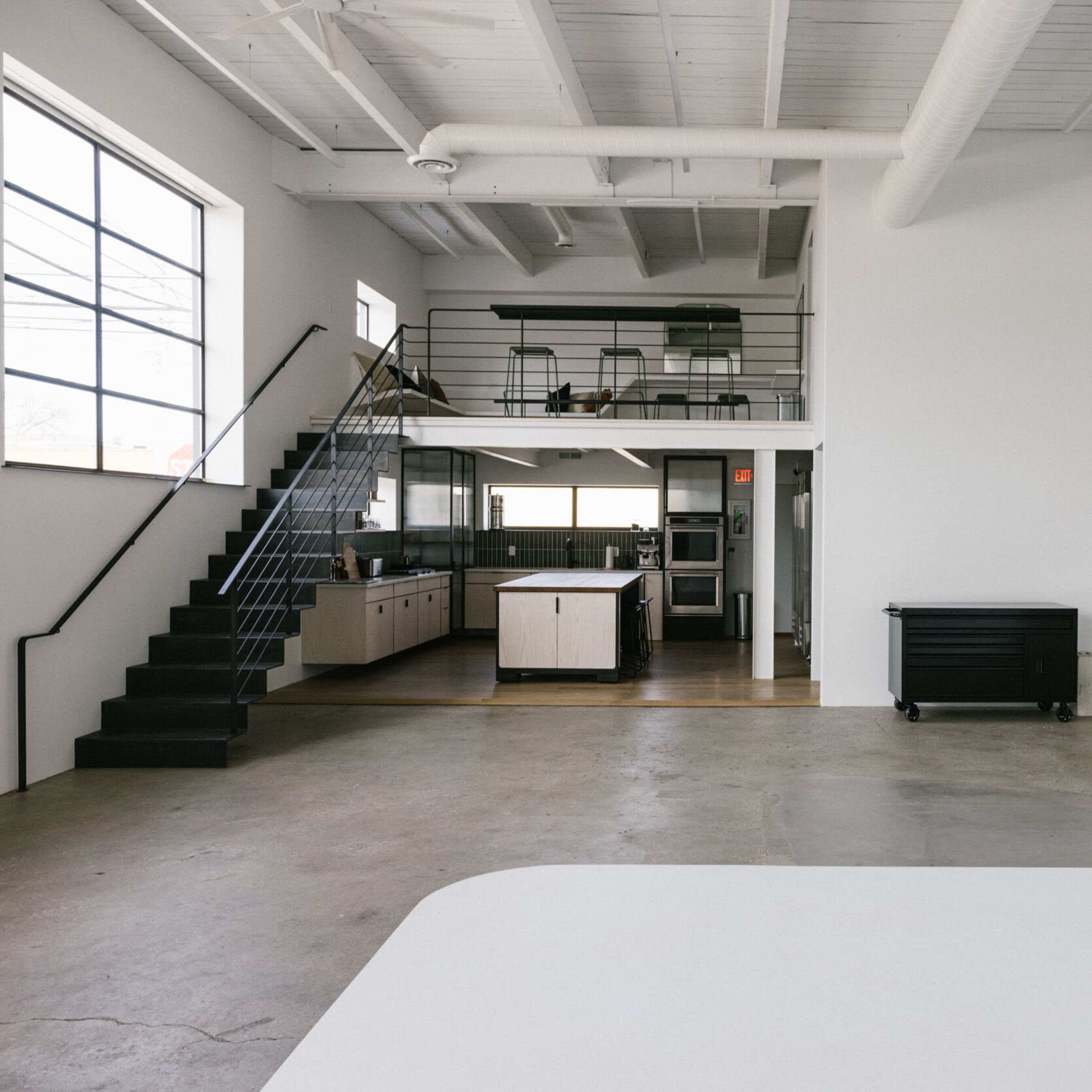 An open, minimalist space featuring a kitchen, staircase, and an area with a large, curved white surface.