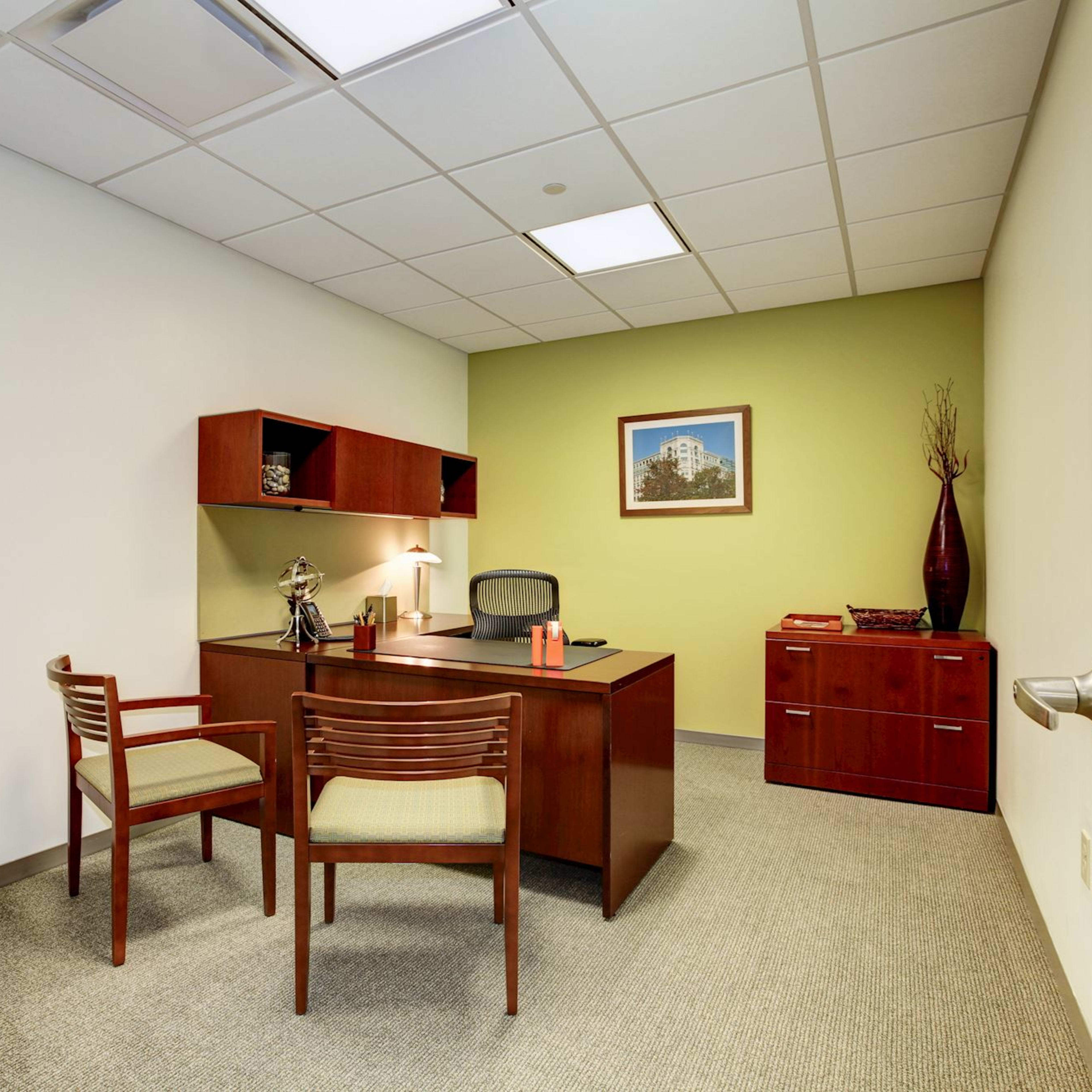 A sparse office space featuring a wooden desk, two chairs, and a green accent wall with a framed picture.