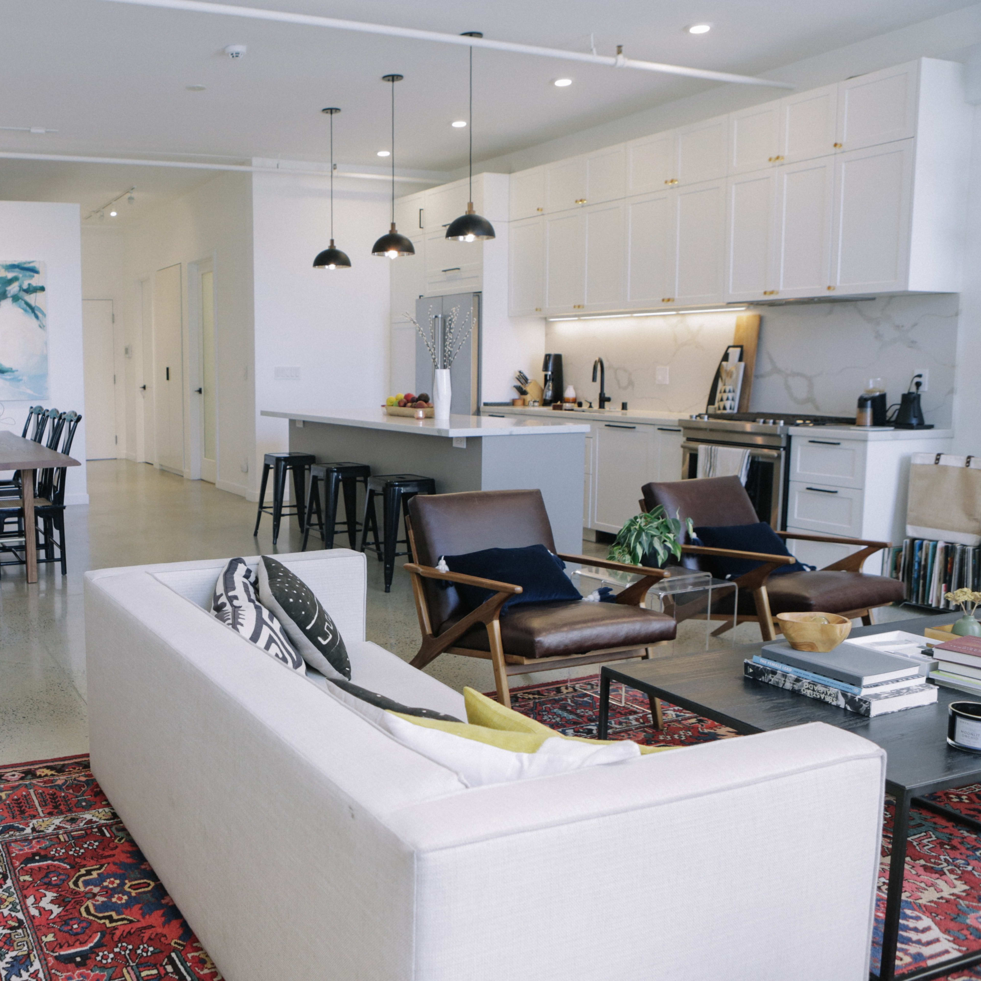 A spacious, modern living area and dining space, featuring a sofa, dining table, and kitchen with elegant cabinetry and industrial-style lighting.