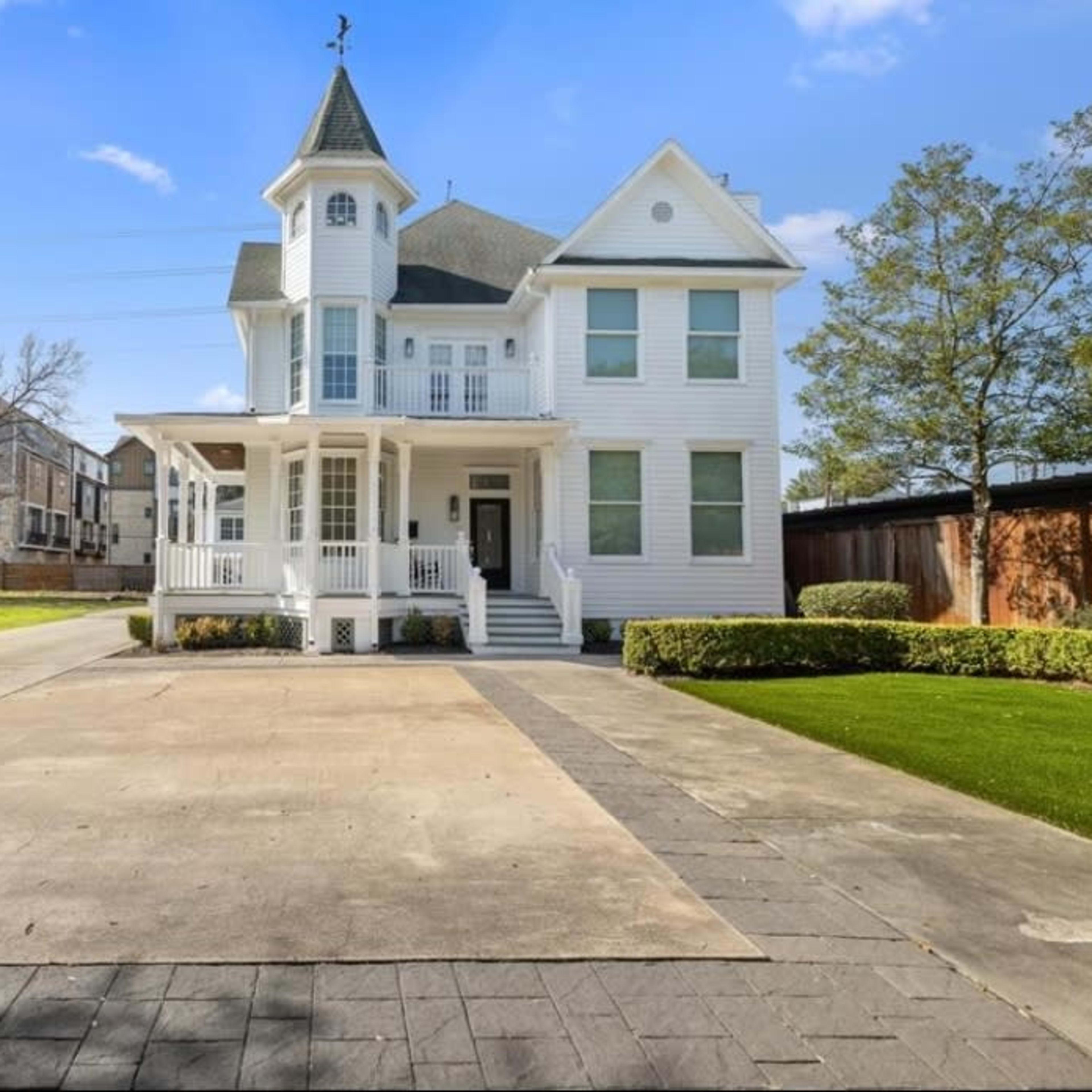 A large, two-story white Victorian-style house with a tower, a covered porch, and a paved driveway.