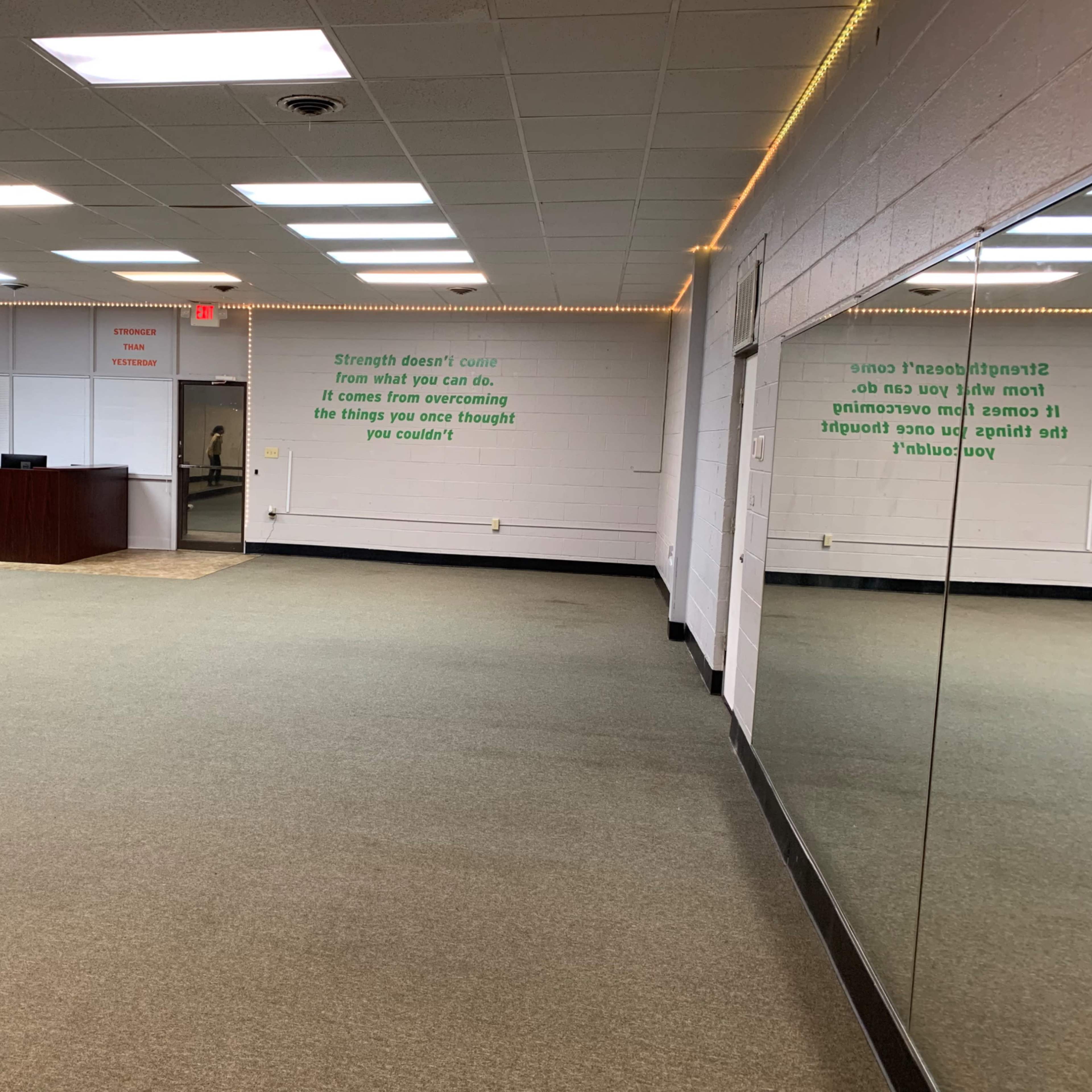 An empty room with carpeted flooring, a reception area in the back, and mirrors on one side featuring motivational quotes on the walls.