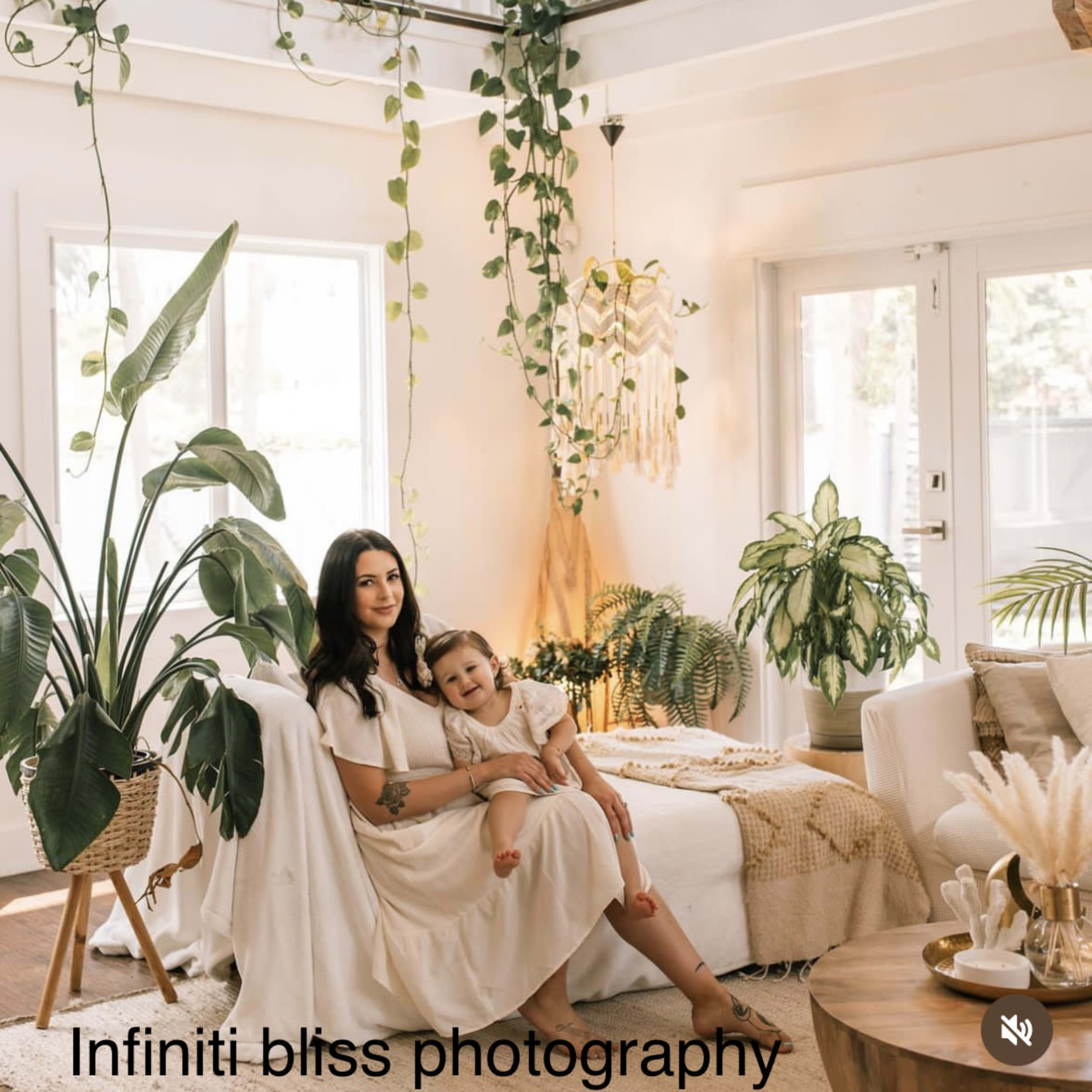 A woman sits on a couch with a child in a well-lit living room adorned with indoor plants and decorative elements.