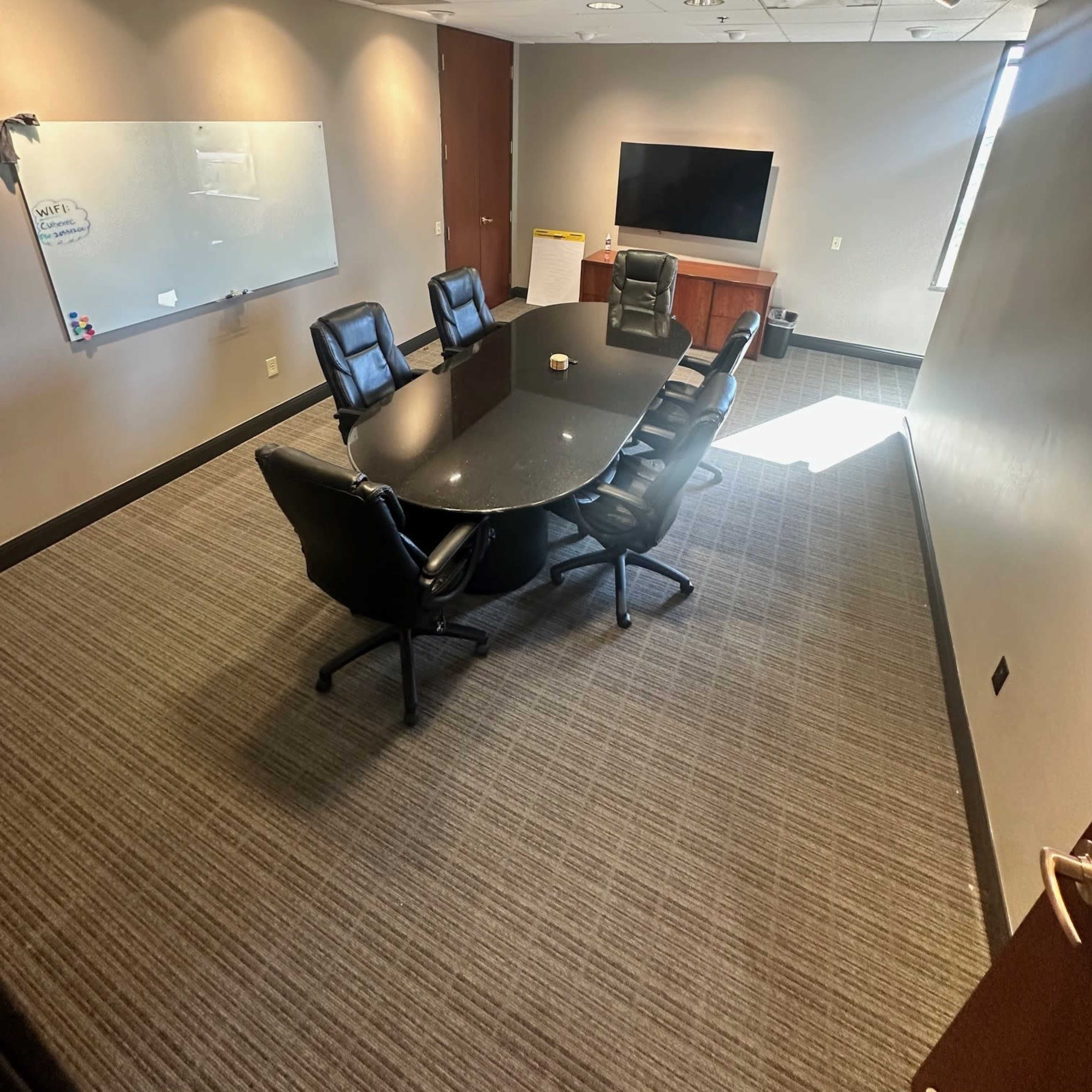 A modern conference room featuring a circular black table surrounded by black leather chairs, with a large screen and a whiteboard on the walls.