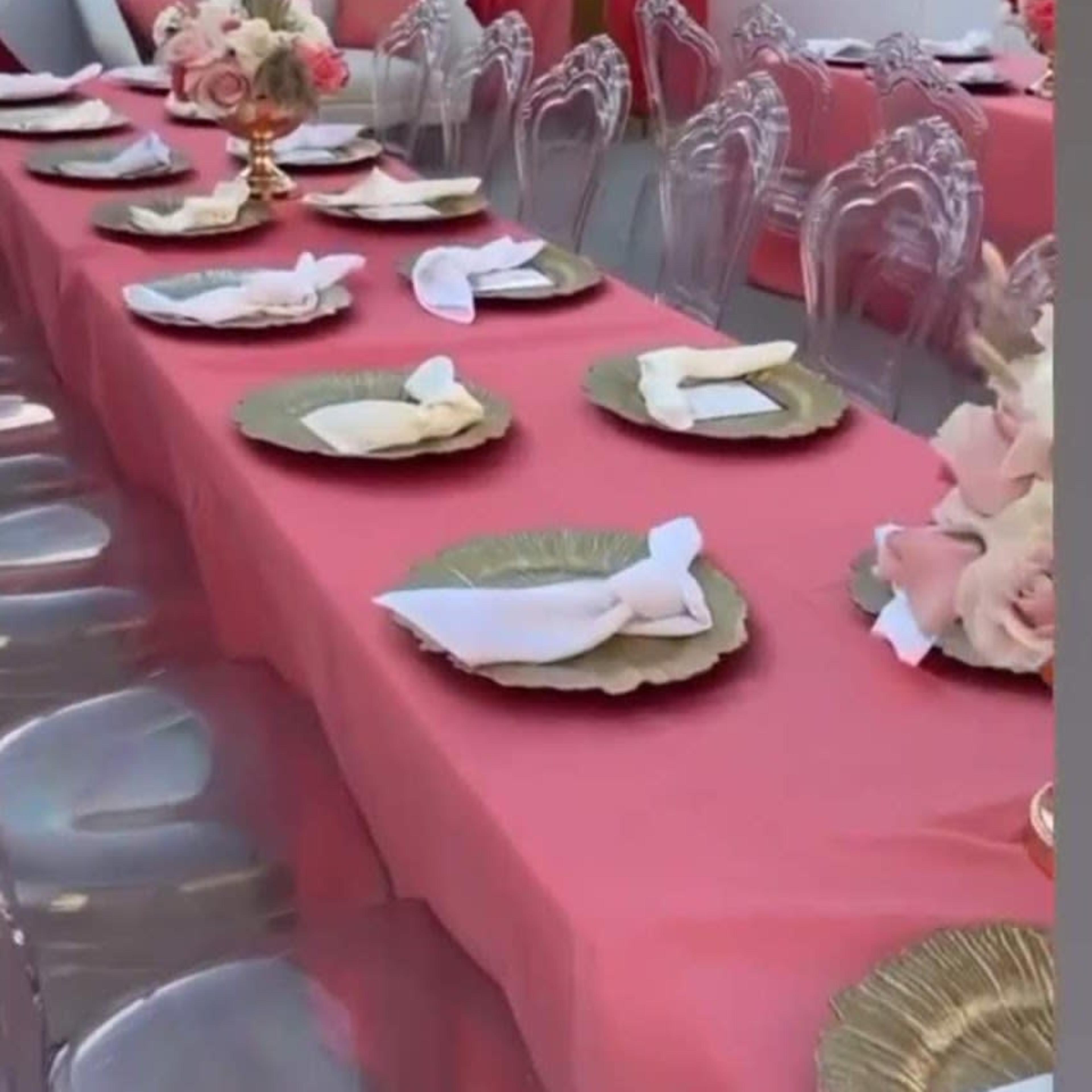 A long table is set with pink tablecloths, clear acrylic chairs, and floral centerpieces for a baby shower celebration.