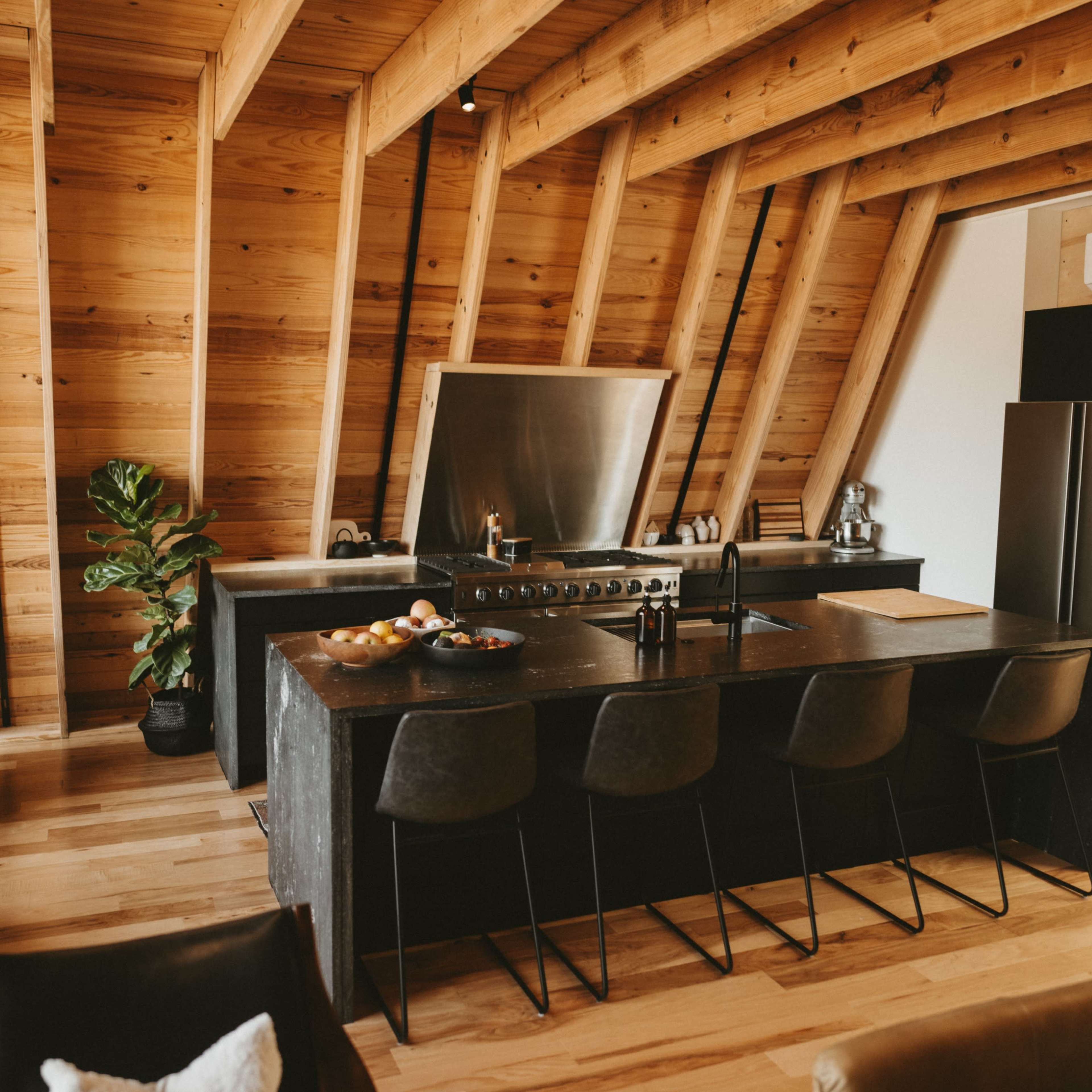 A modern kitchen features a large black island with bar seating, stainless steel appliances, and wooden beams in the ceiling.