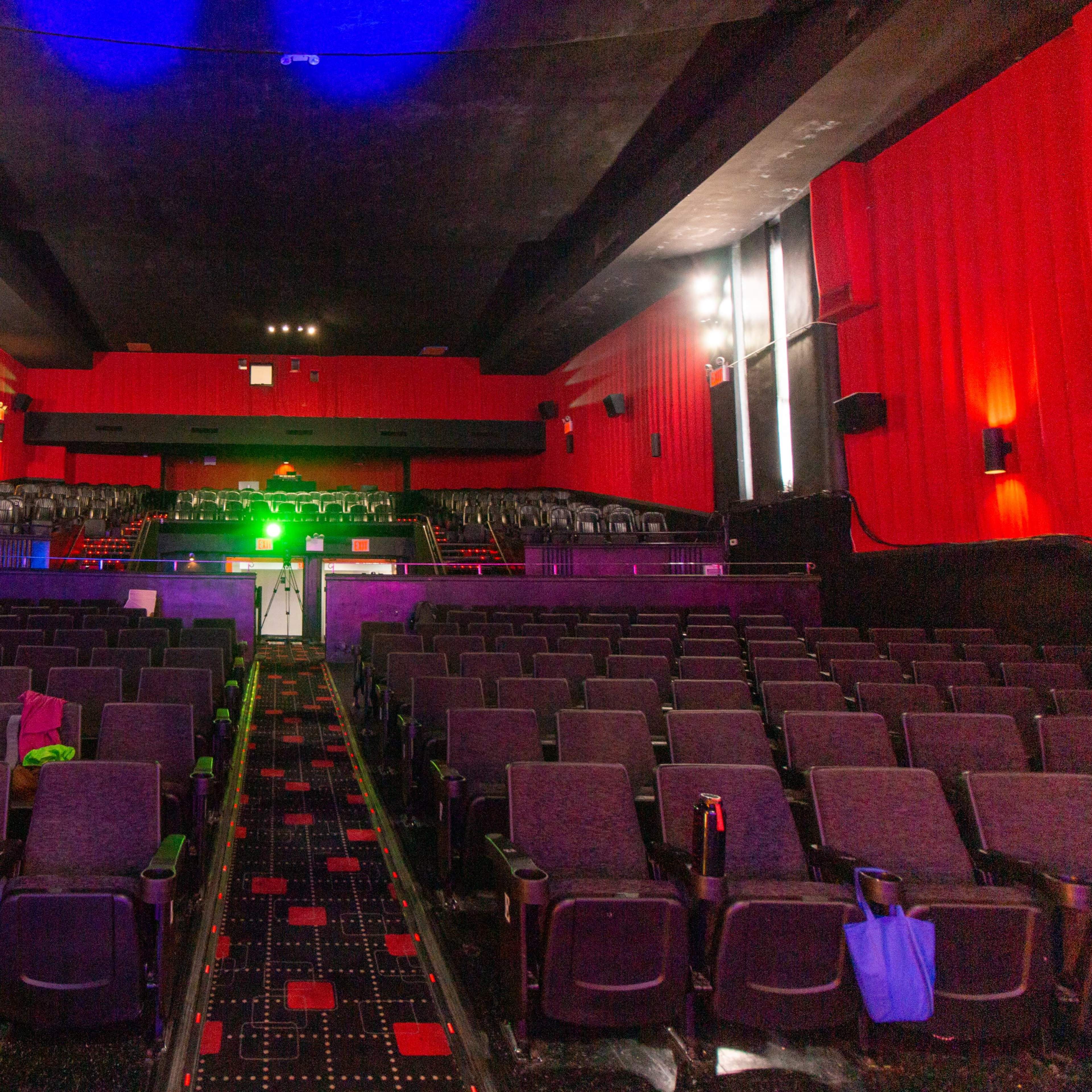 An empty movie theater with red walls, several rows of black seats, and a stage illuminated by green light.