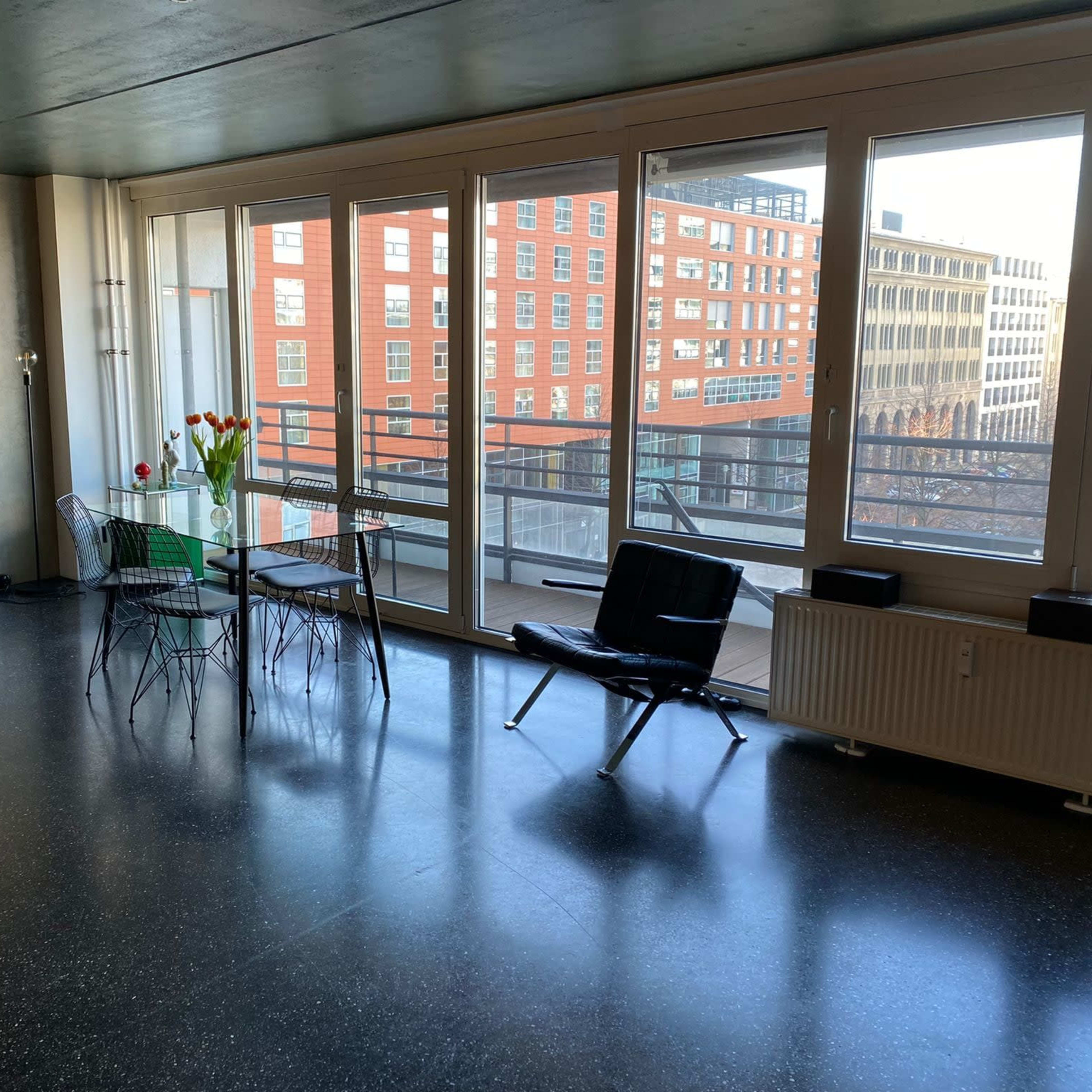 A modern interior space with large windows, a dining table with chairs, and a black sofa.