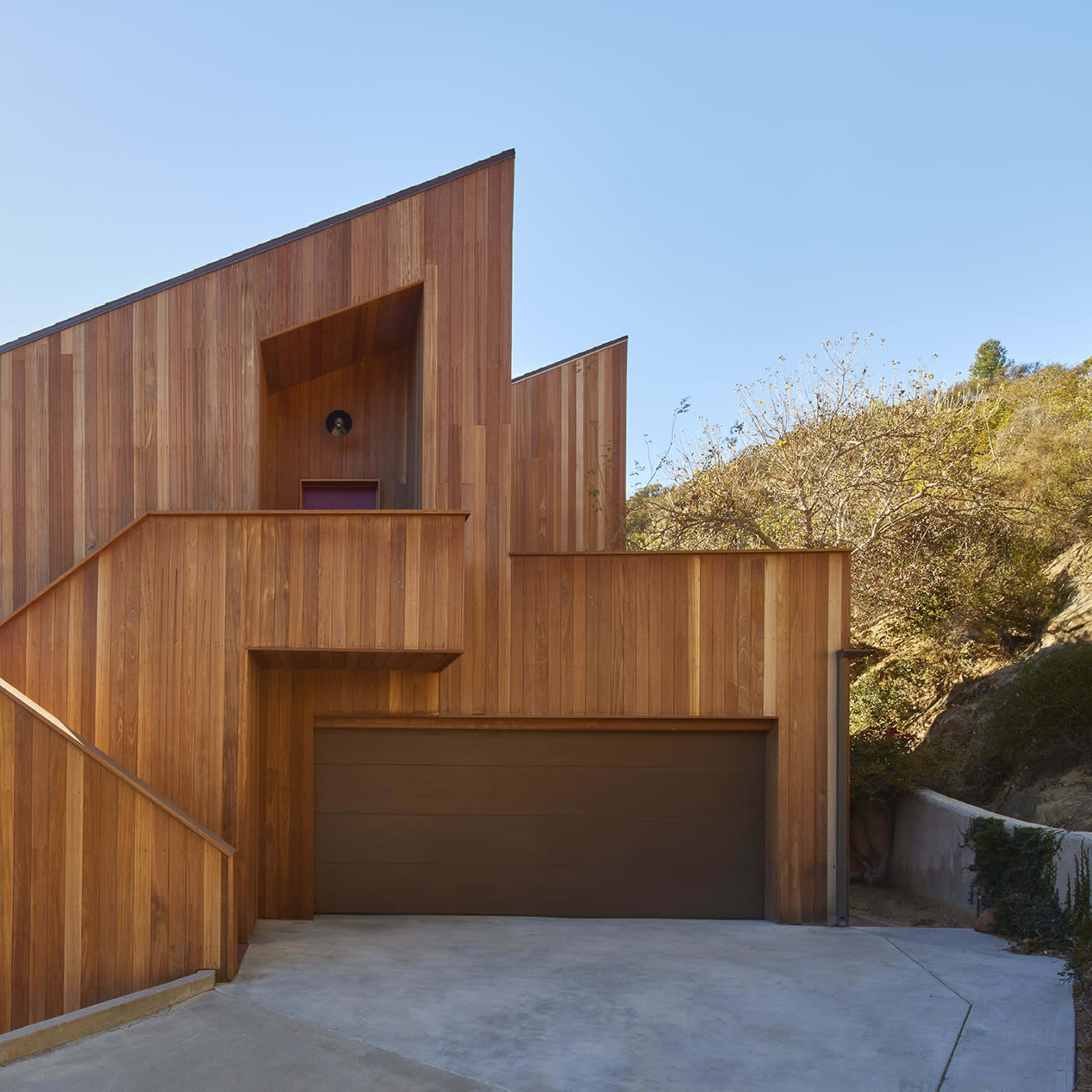 A modern wooden house with a geometric design, featuring slanted walls and a garage at the base.