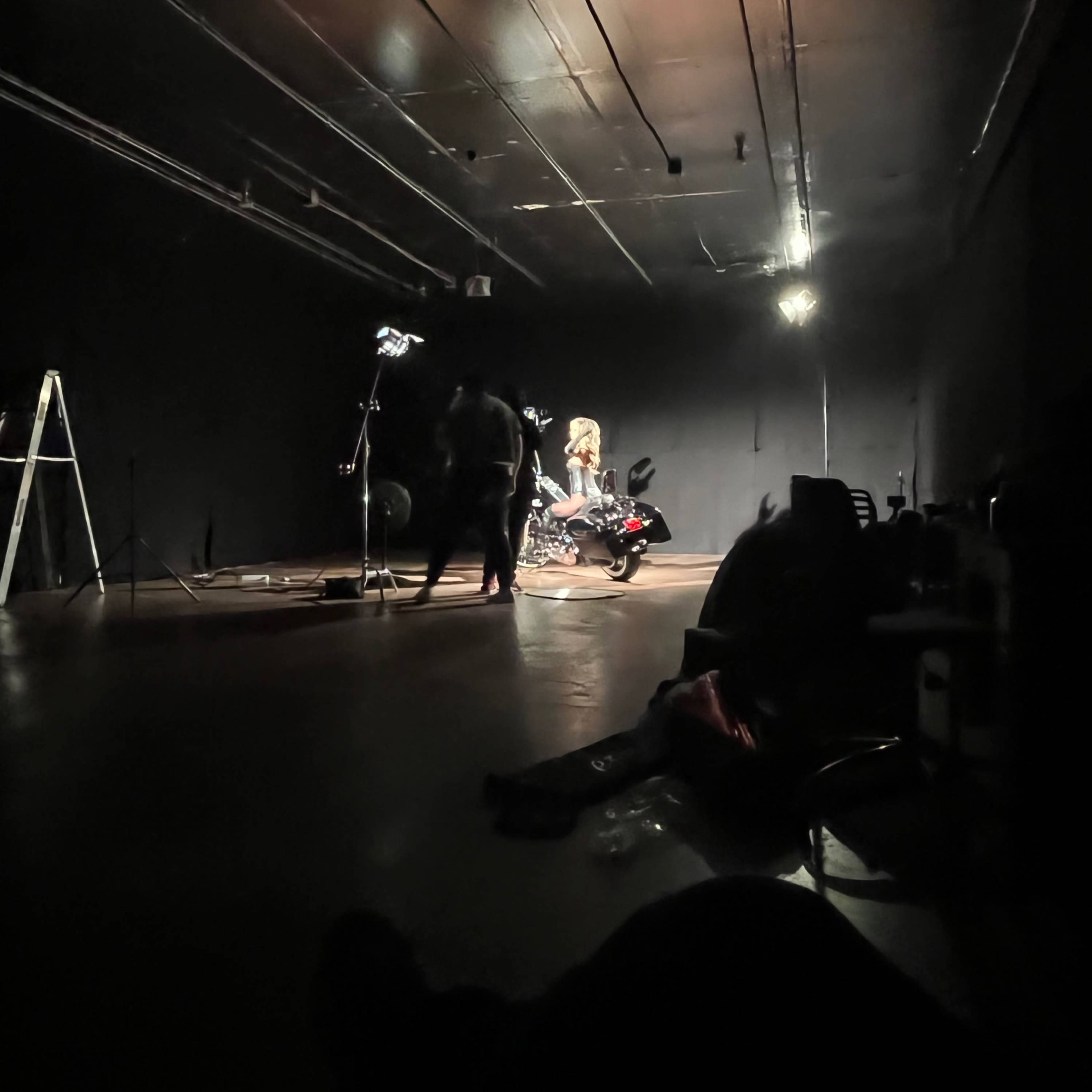 A person sits on a motorcycle in a dimly lit studio, surrounded by professional lighting equipment.