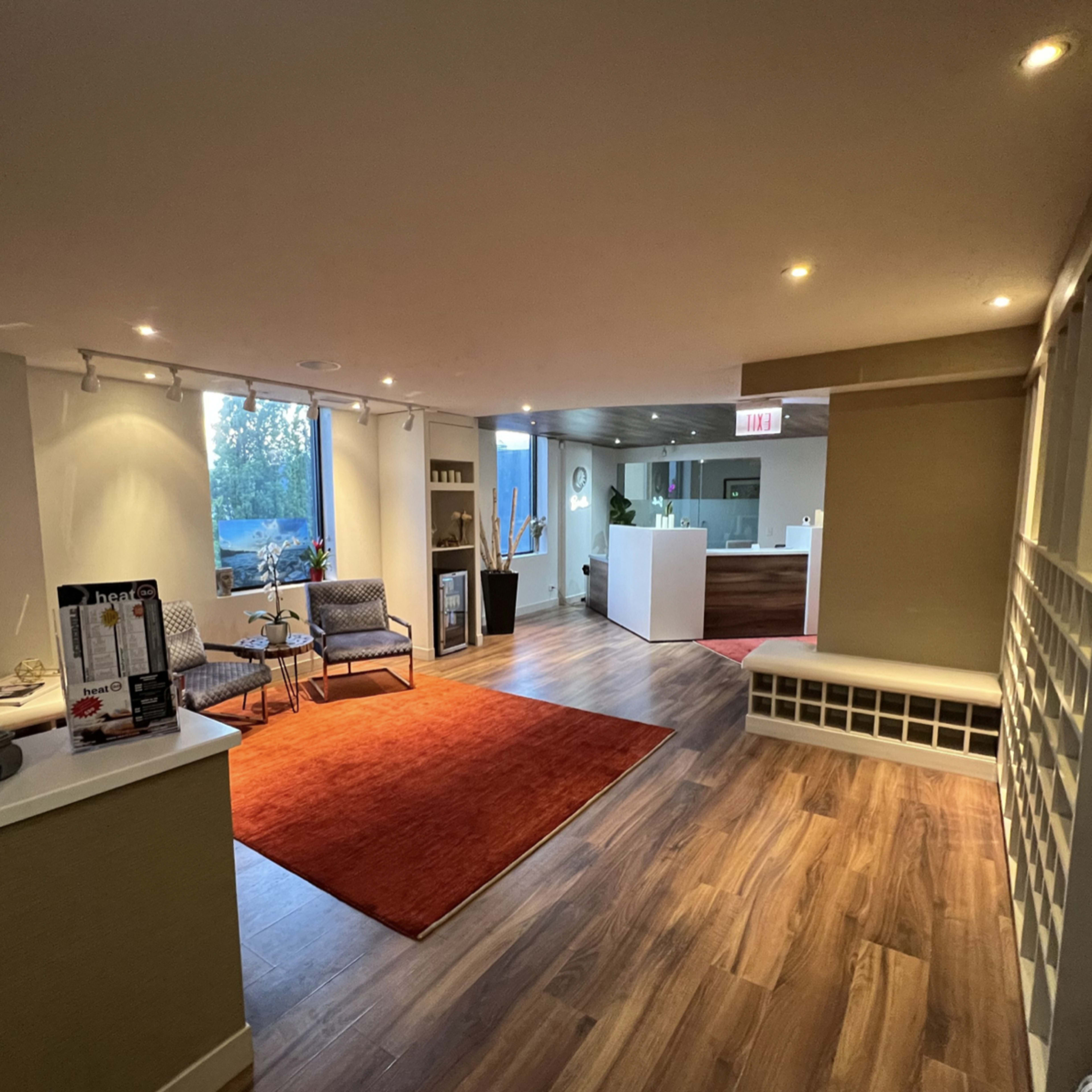 A spacious, well-lit reception area with wooden flooring, a red area rug, seating, and decorative sculptures.