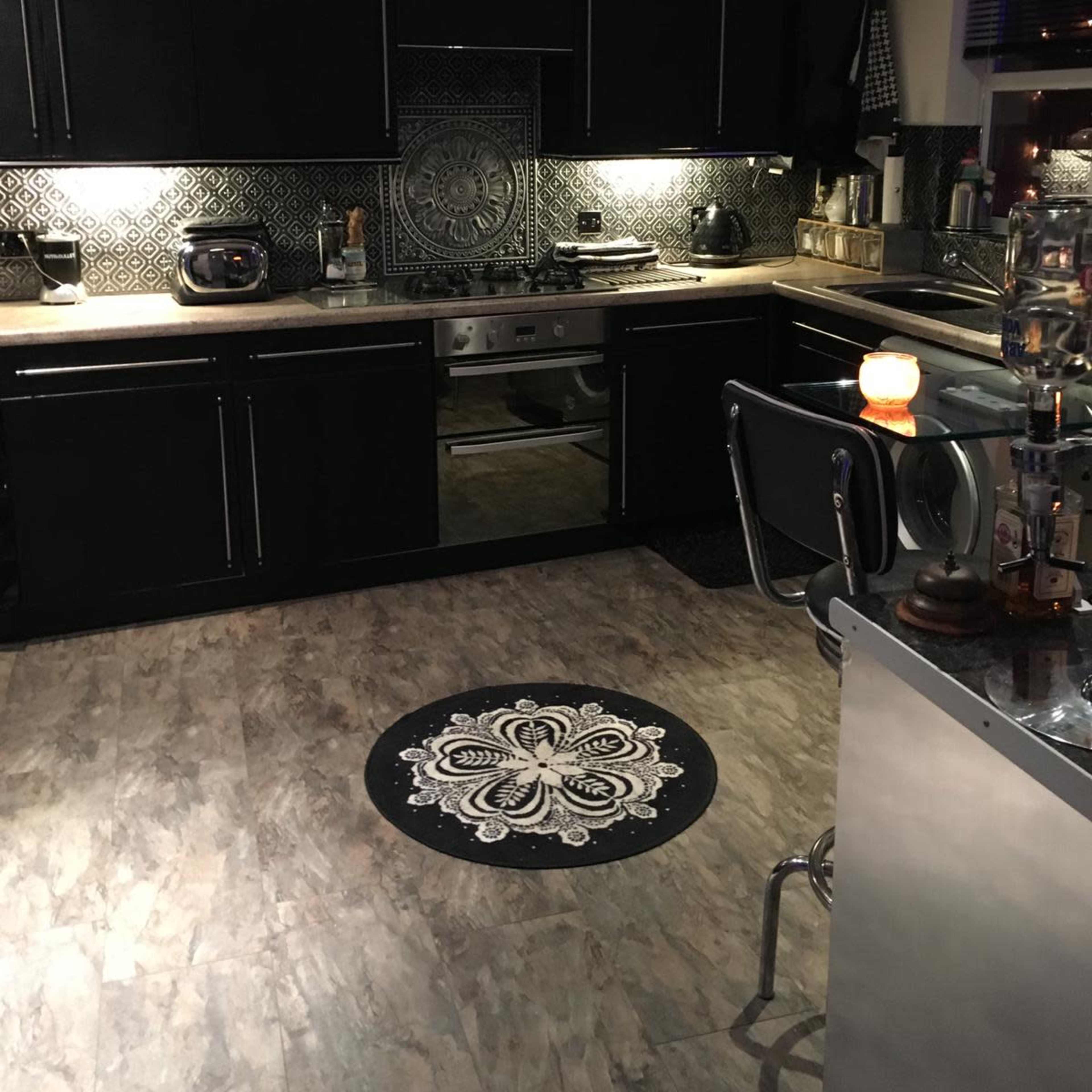 A modern kitchen with black cabinetry, a patterned backsplash, and a round rug on the floor.
