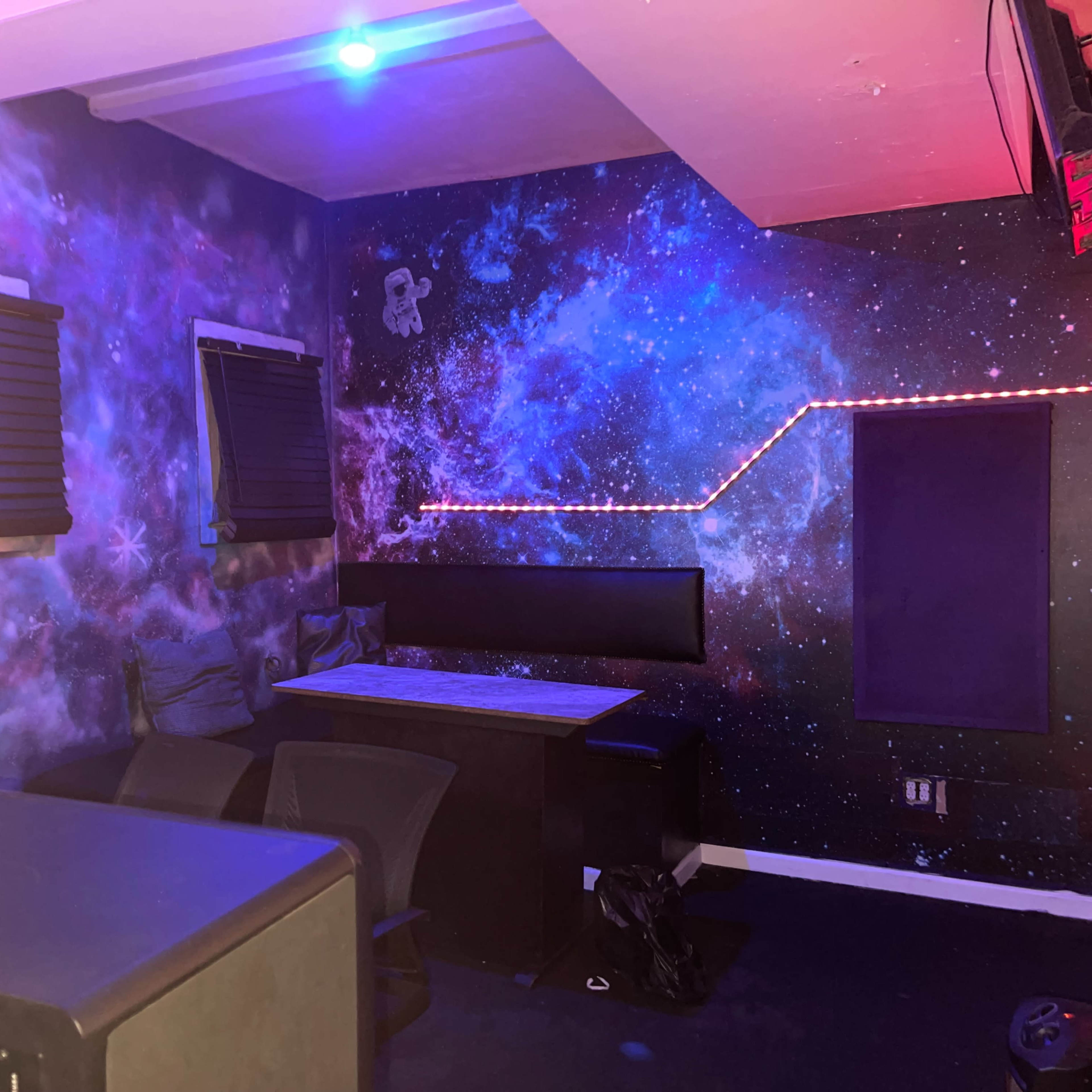 A room with galaxy-themed walls, a table, and chairs positioned against one side.