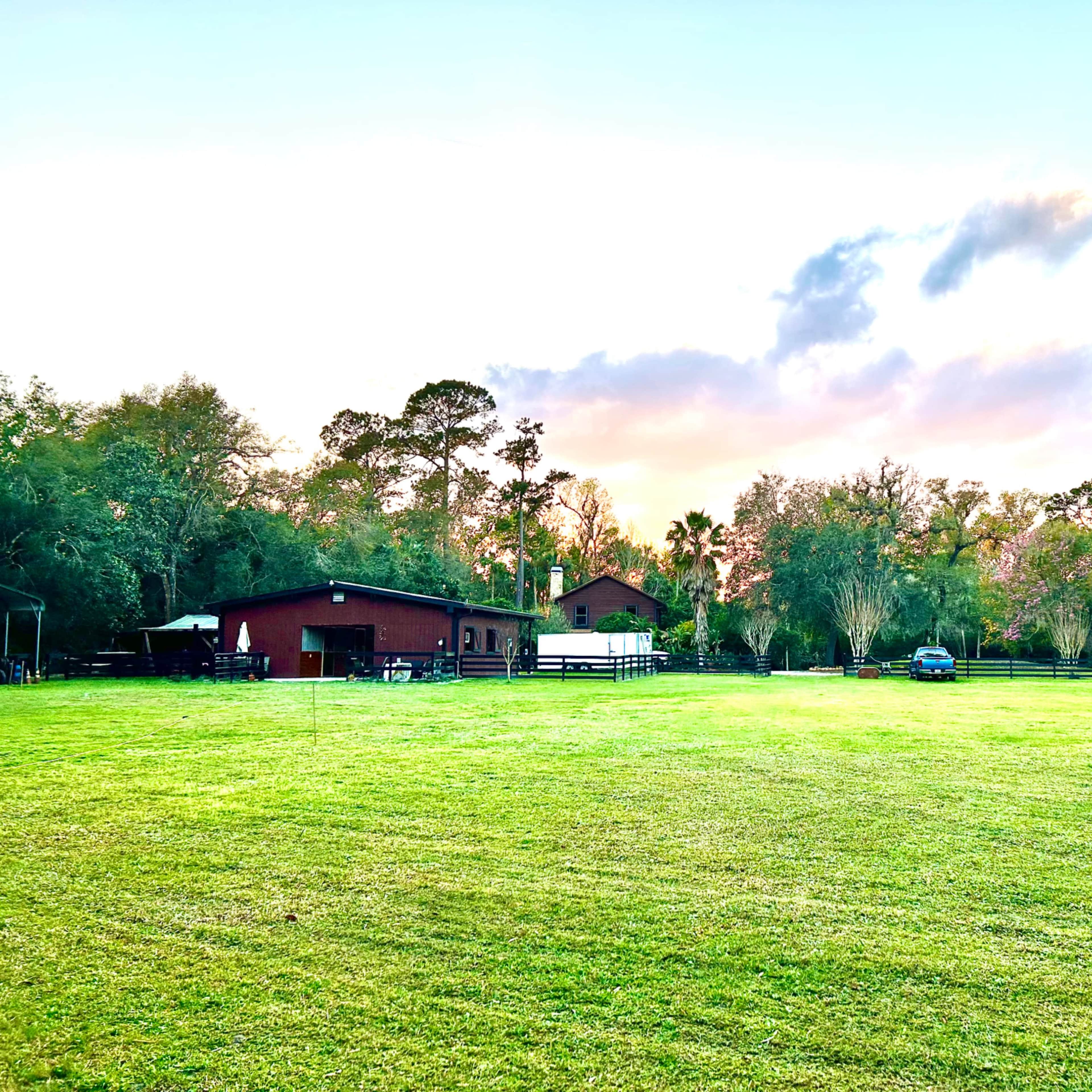 A large grassy area features a red barn and a white structure, surrounded by trees and a blue sky with scattered clouds.