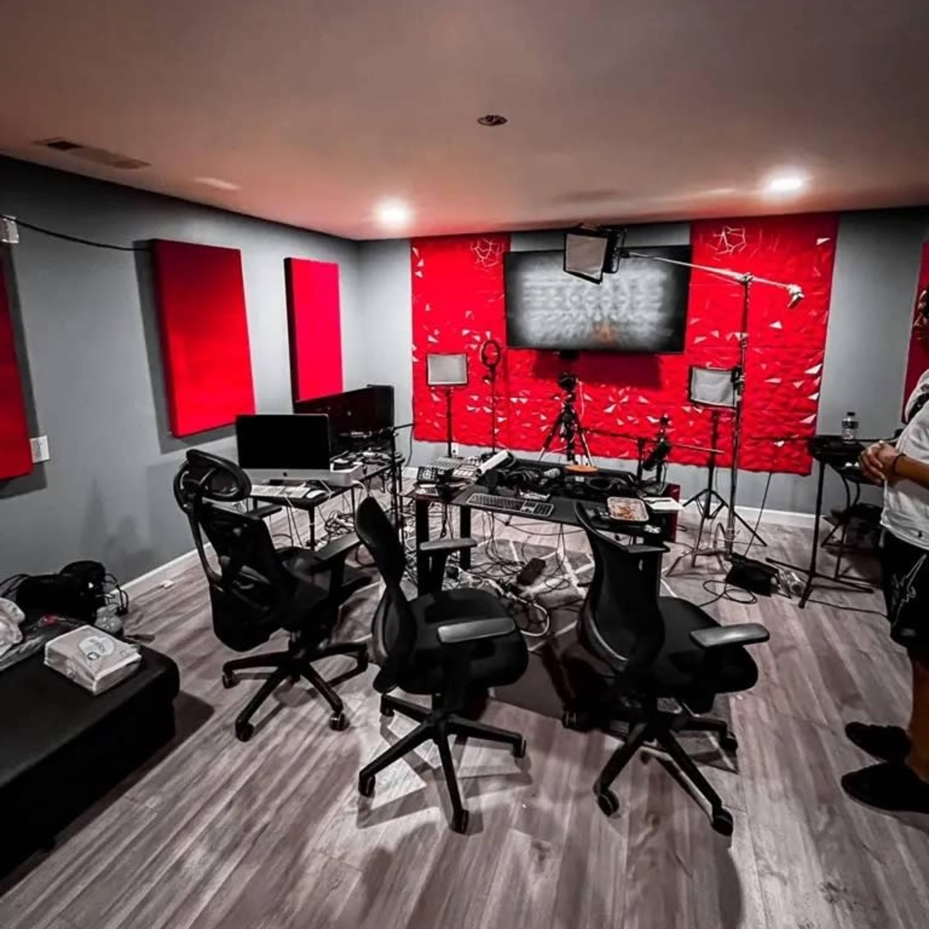 A recording studio featuring multiple chairs, monitors, and lighting equipment against a backdrop of red acoustic panels.