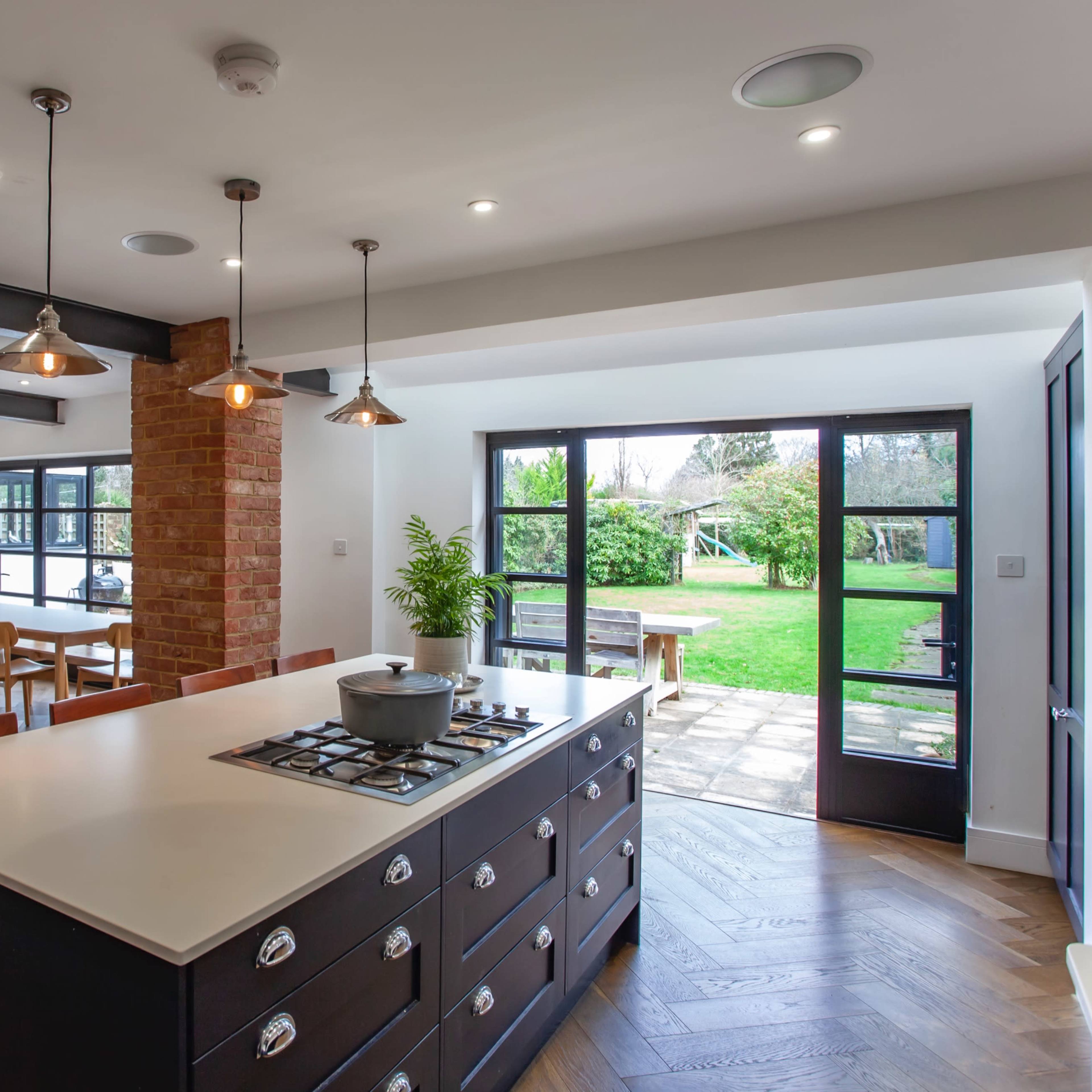 A modern kitchen with a large island and a view of an outdoor garden area, featuring a mix of wooden and brick elements.