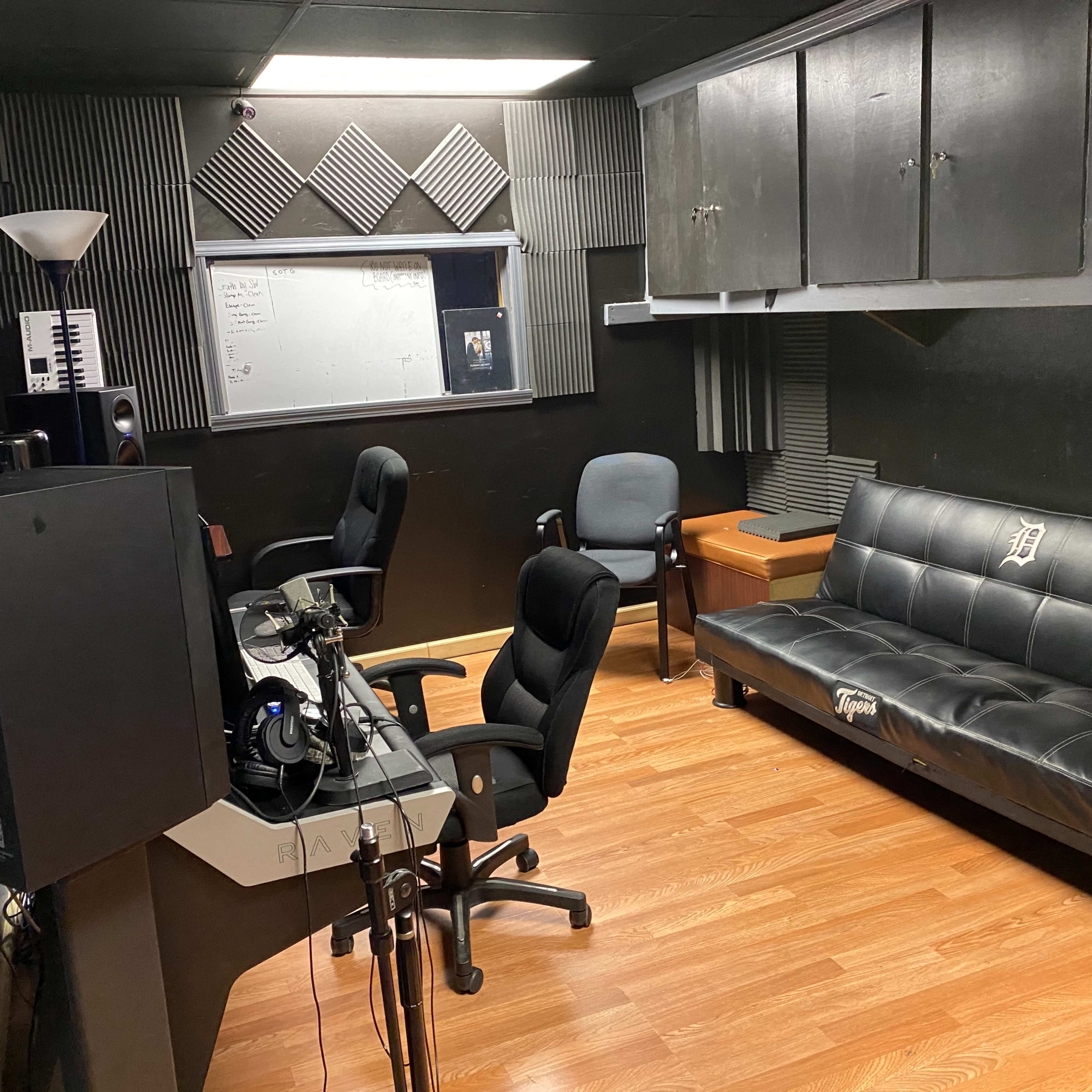 A music studio featuring a black futon, several audio monitors, and a desk with computer equipment.