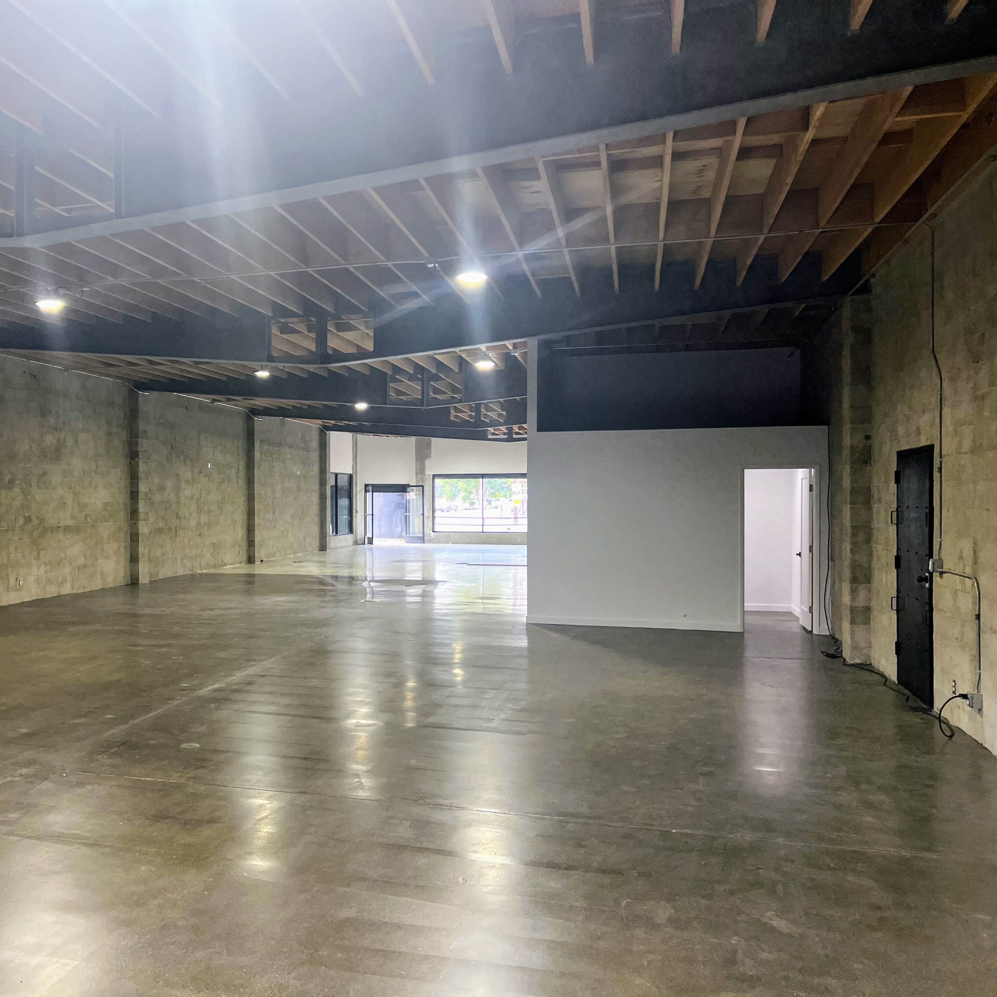 A spacious industrial interior with concrete walls and a polished floor, featuring large windows on one side.