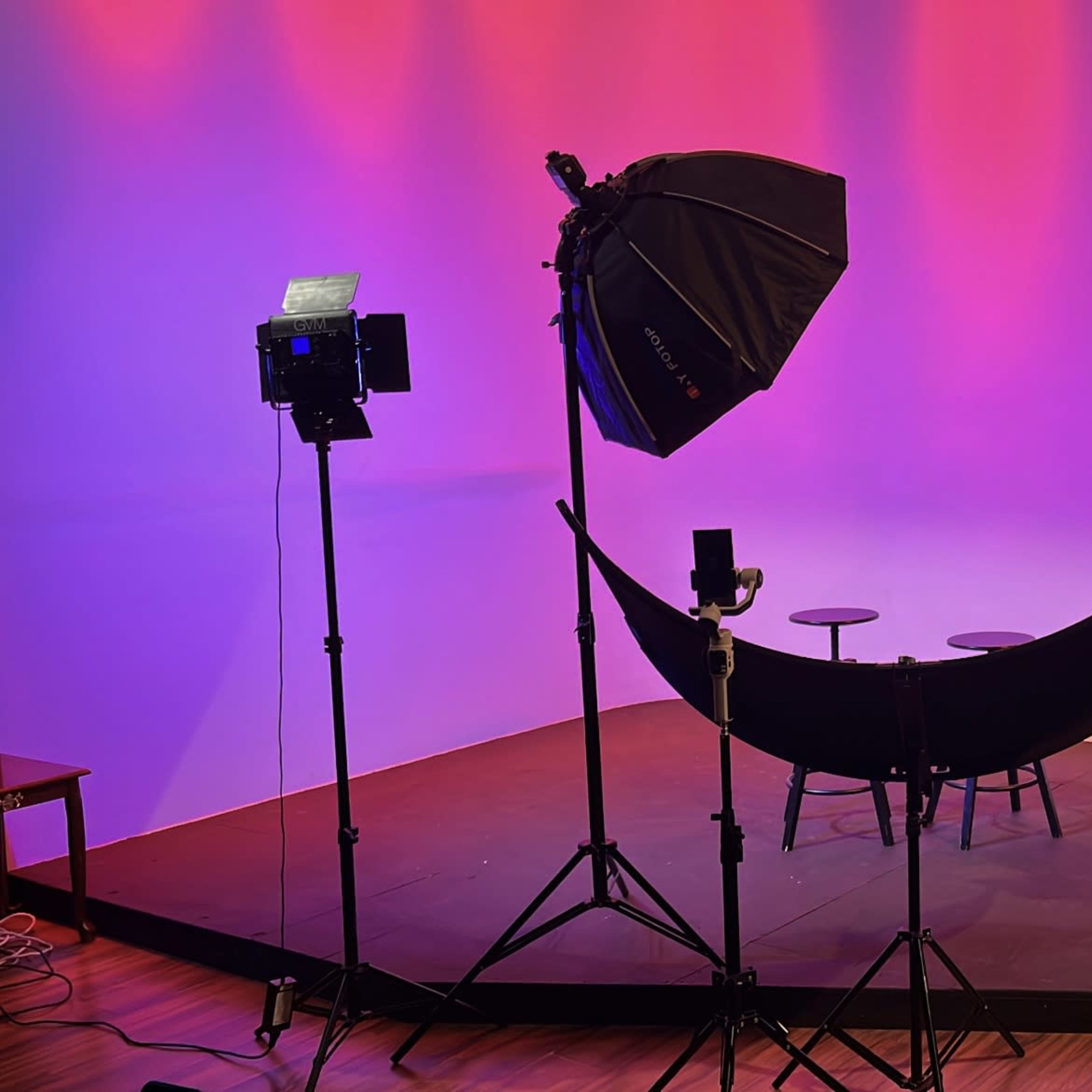 A photography studio setup with two light stands, a large softbox, a backdrop, and two stools on a raised platform.