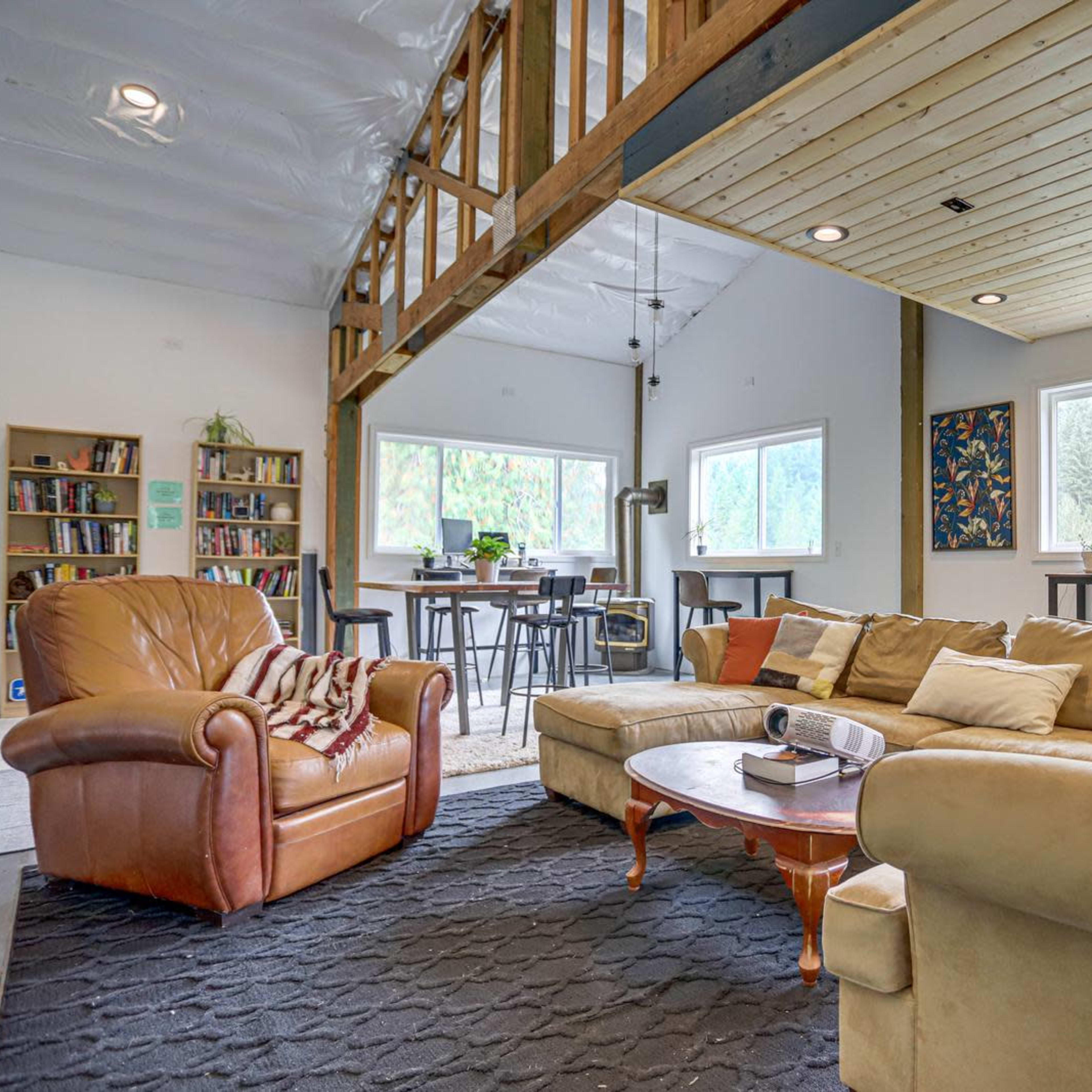 A spacious living area featuring a large sofa, an armchair, a coffee table, and a bookshelf, with large windows that provide natural light.