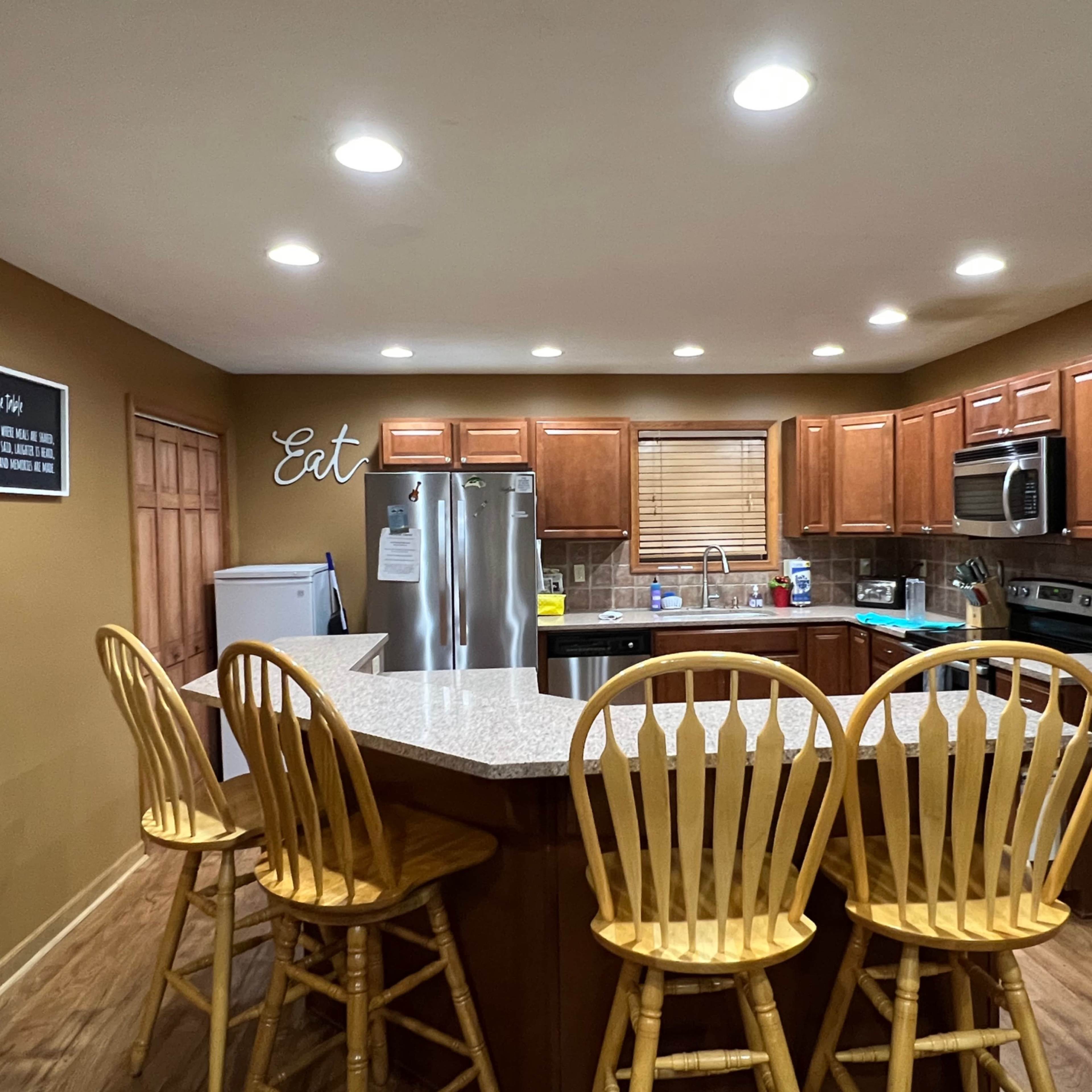 The kitchen features wooden cabinets, stainless steel appliances, and a large island with four wooden bar stools.