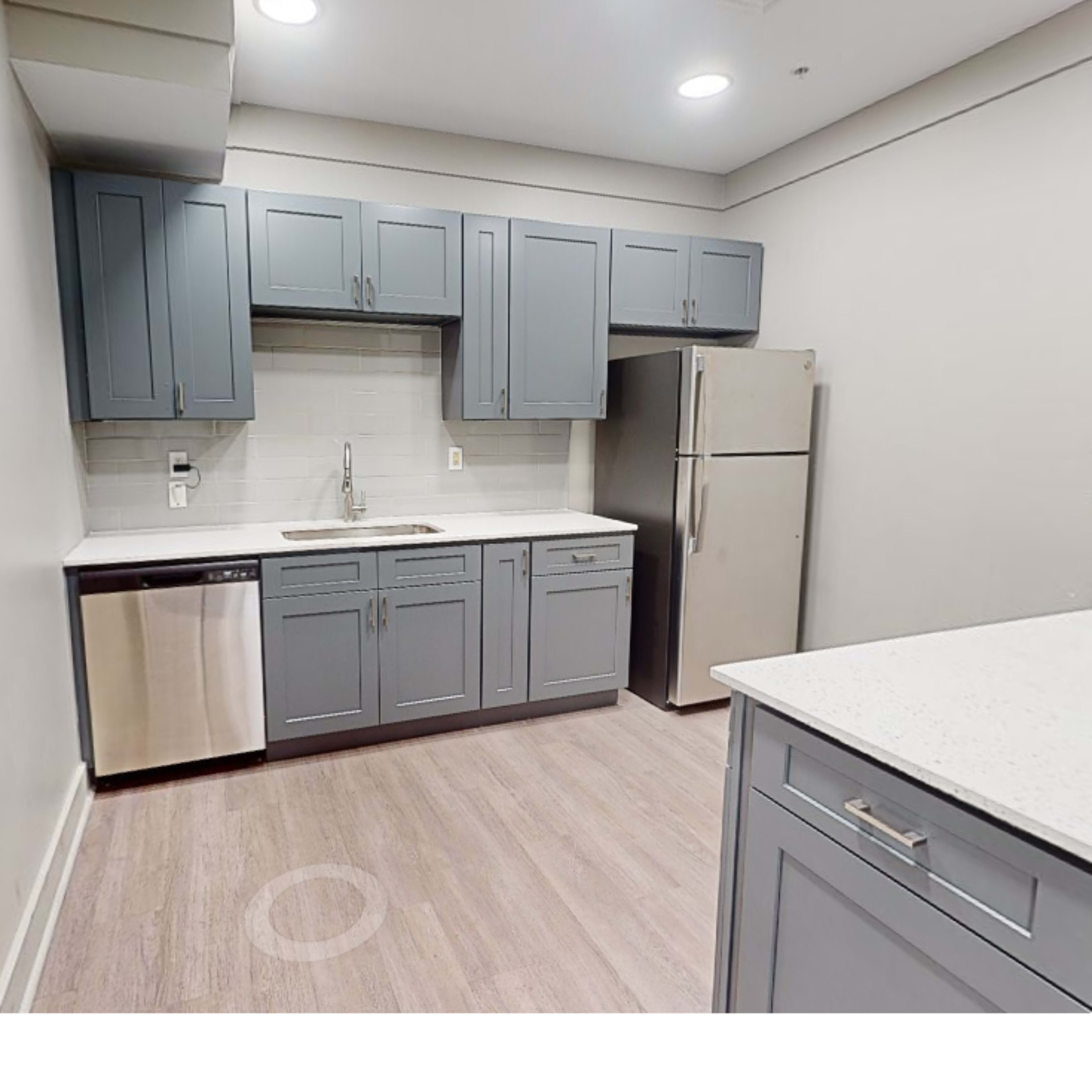 A modern kitchen with gray cabinets, a stainless steel refrigerator, a dishwasher, and a white countertop.