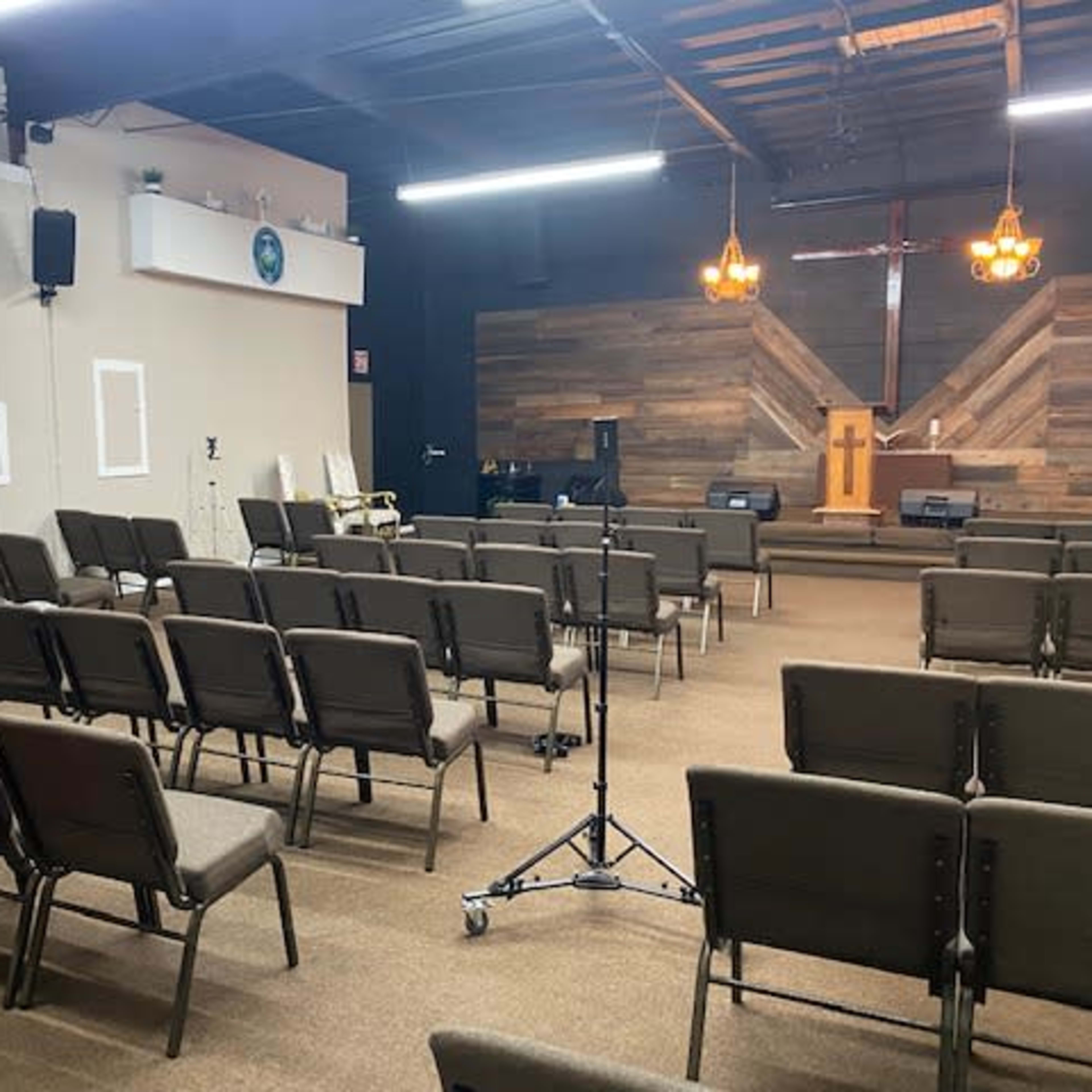 An empty church interior featuring rows of chairs facing a wooden platform with a cross and a few musical instruments.