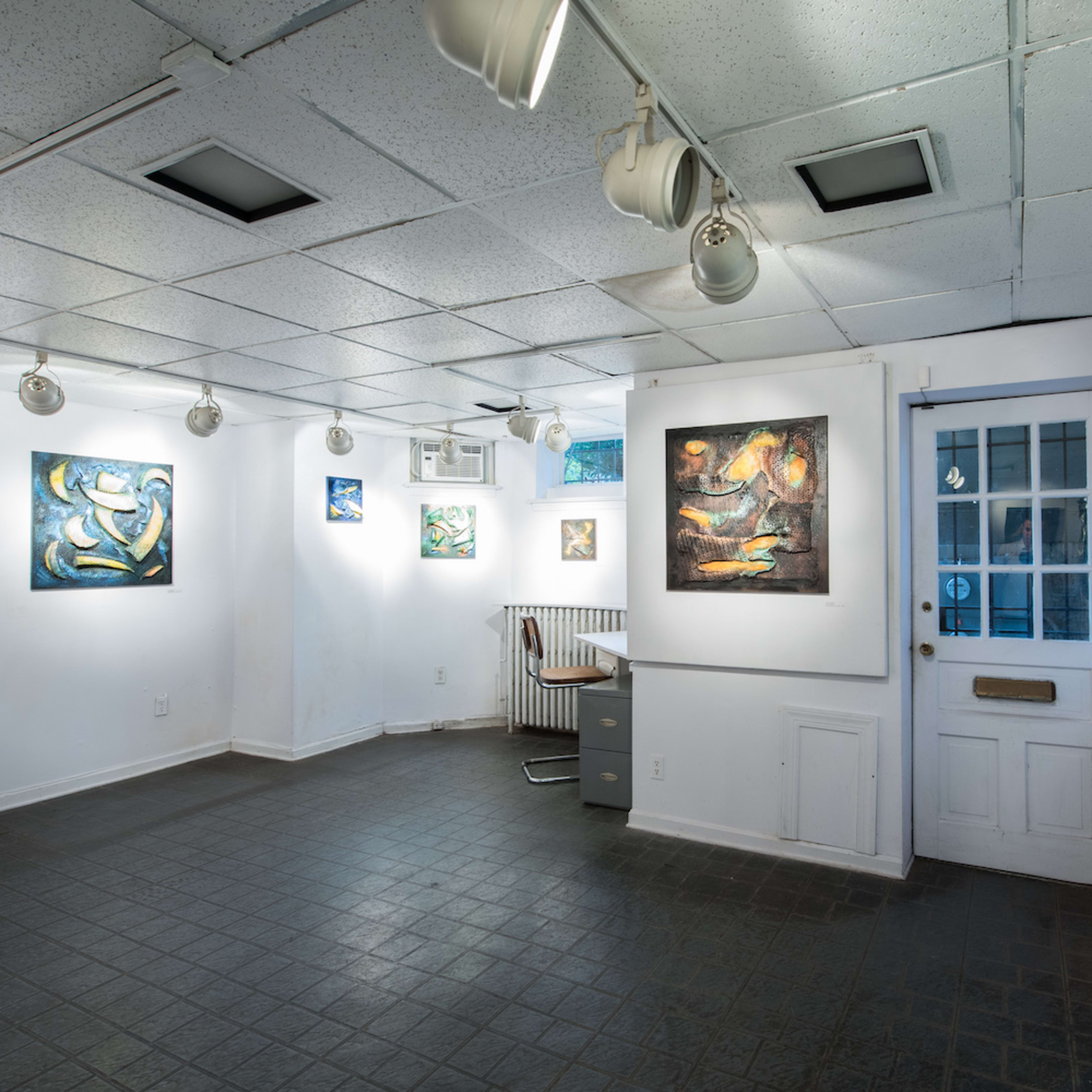 An art gallery with artworks displayed on white walls, a door on the right, and a desk in the corner.