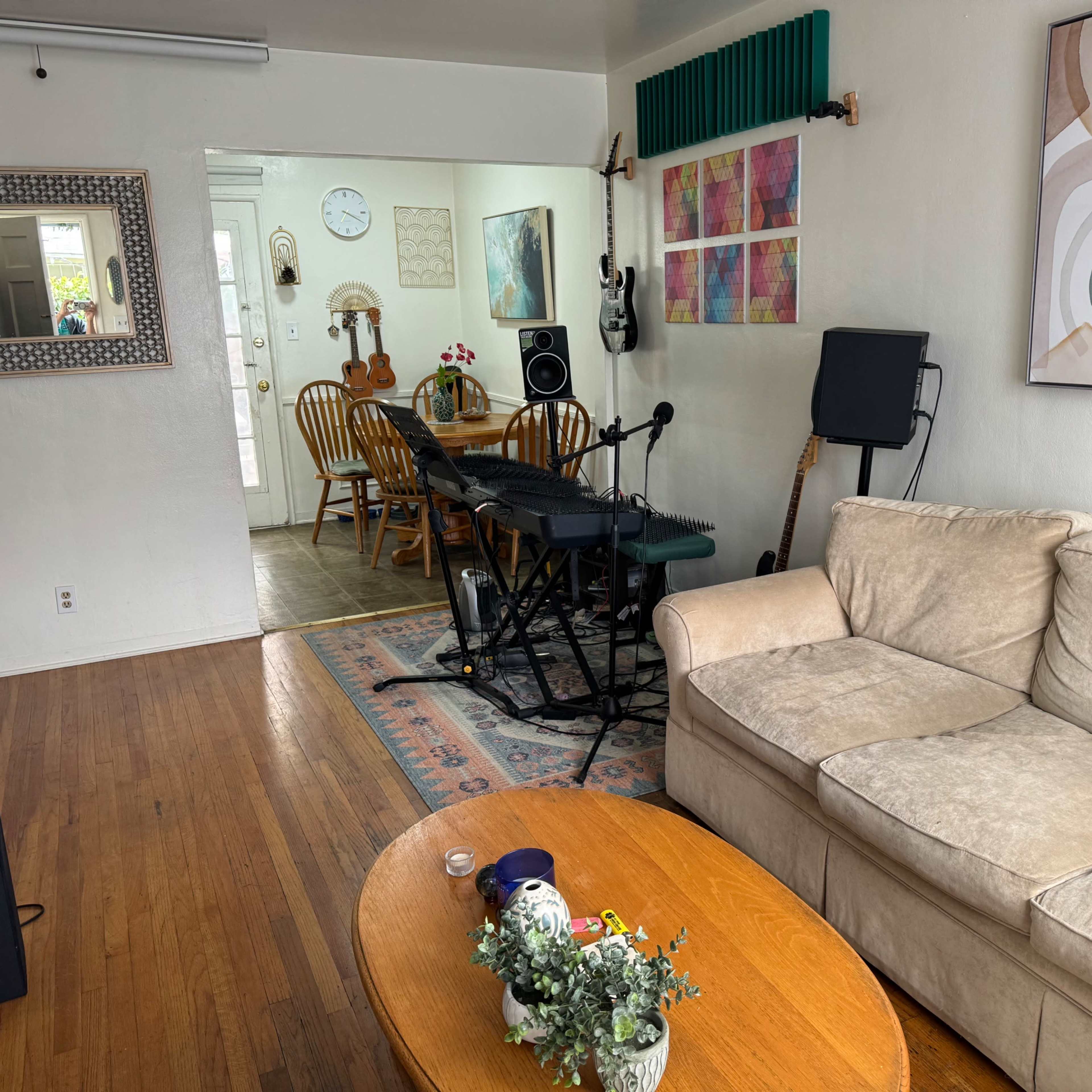 A living room with a beige couch, a wooden coffee table, and a keyboard set up near a dining area that has wooden chairs and a table.