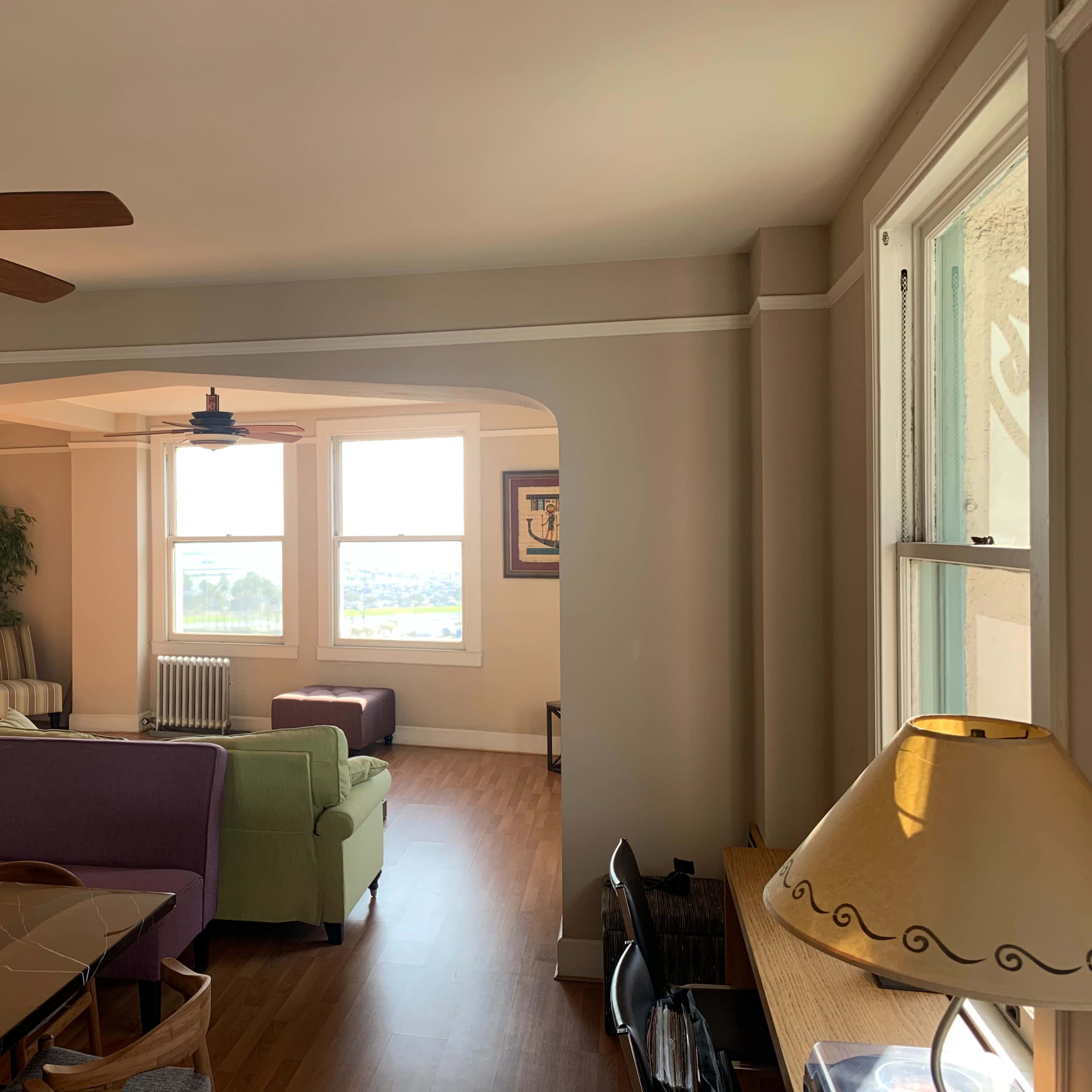 A bright living room features an archway, ceiling fans, and various seating arrangements near windows that overlook a scenic view.